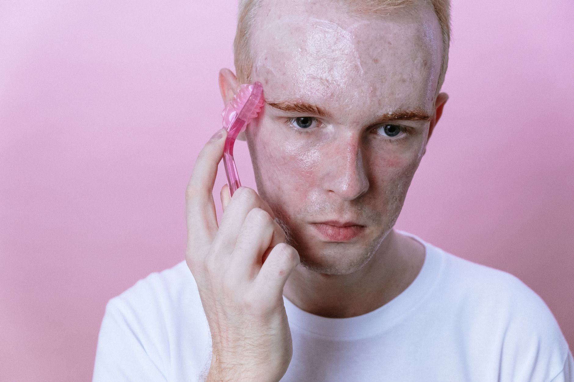 Young person using a pink facial roller in a skincare routine.