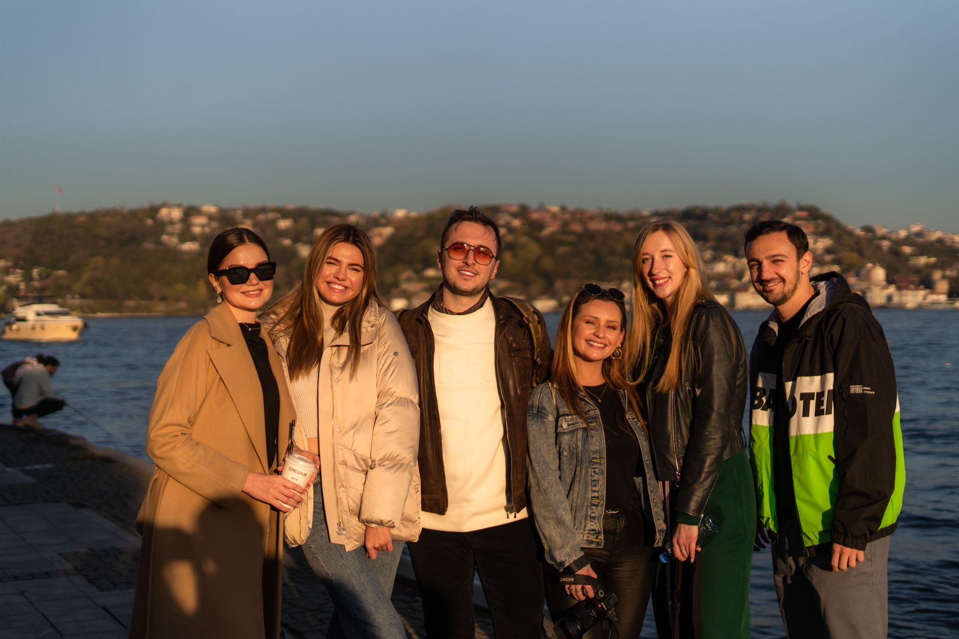 A group of six friends posing happily by the Bosphorus at sunset in Istanbul.