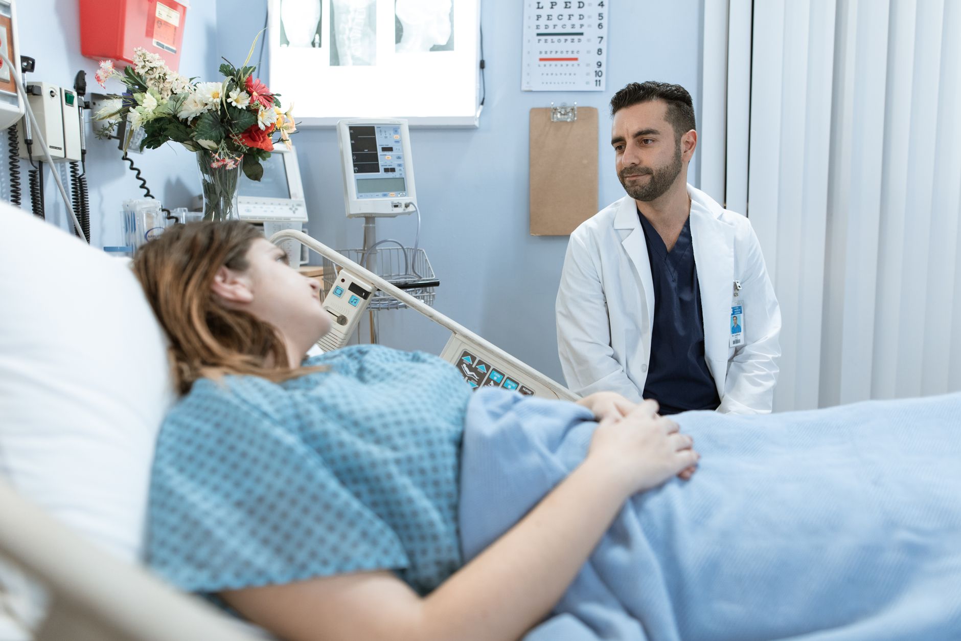 A doctor in a white coat consults with a patient in a hospital room.