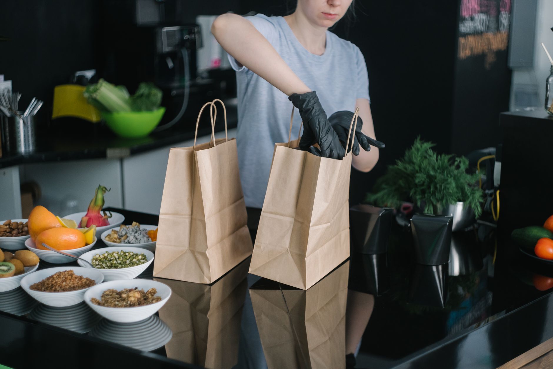 A person in gloves packing nutritious meal components into paper bags in a modern kitchen.