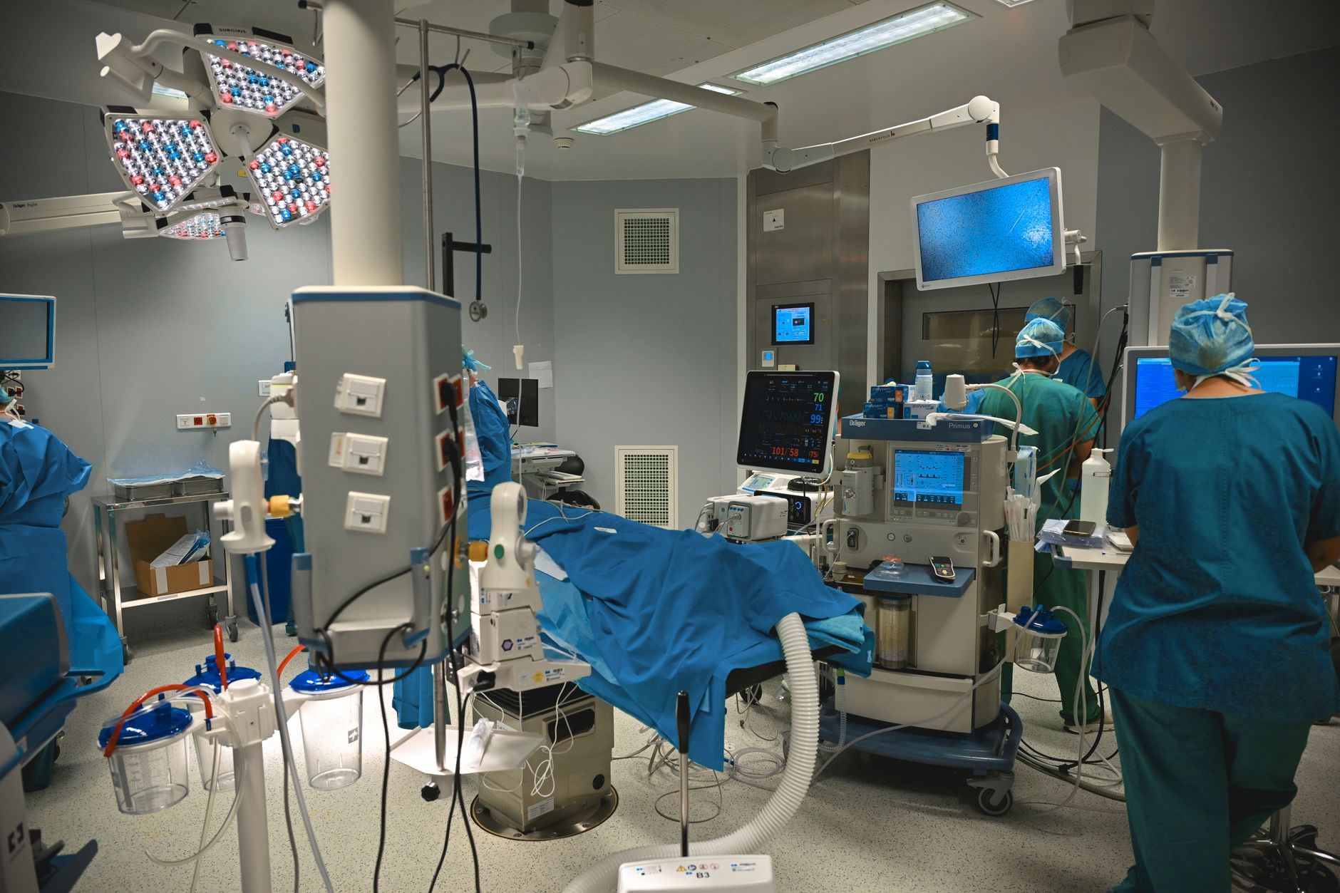 An operating room with monitors and medical equipment; an anesthesiologist reviews vital signs during a procedure.