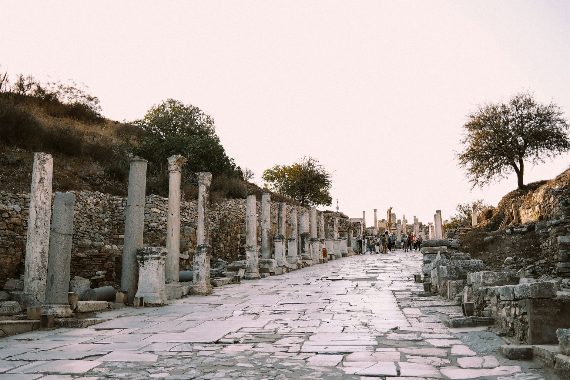 Efes'te sütunlarla çevrili antik cilalı mermer sokakta yürüyen ziyaretçiler.