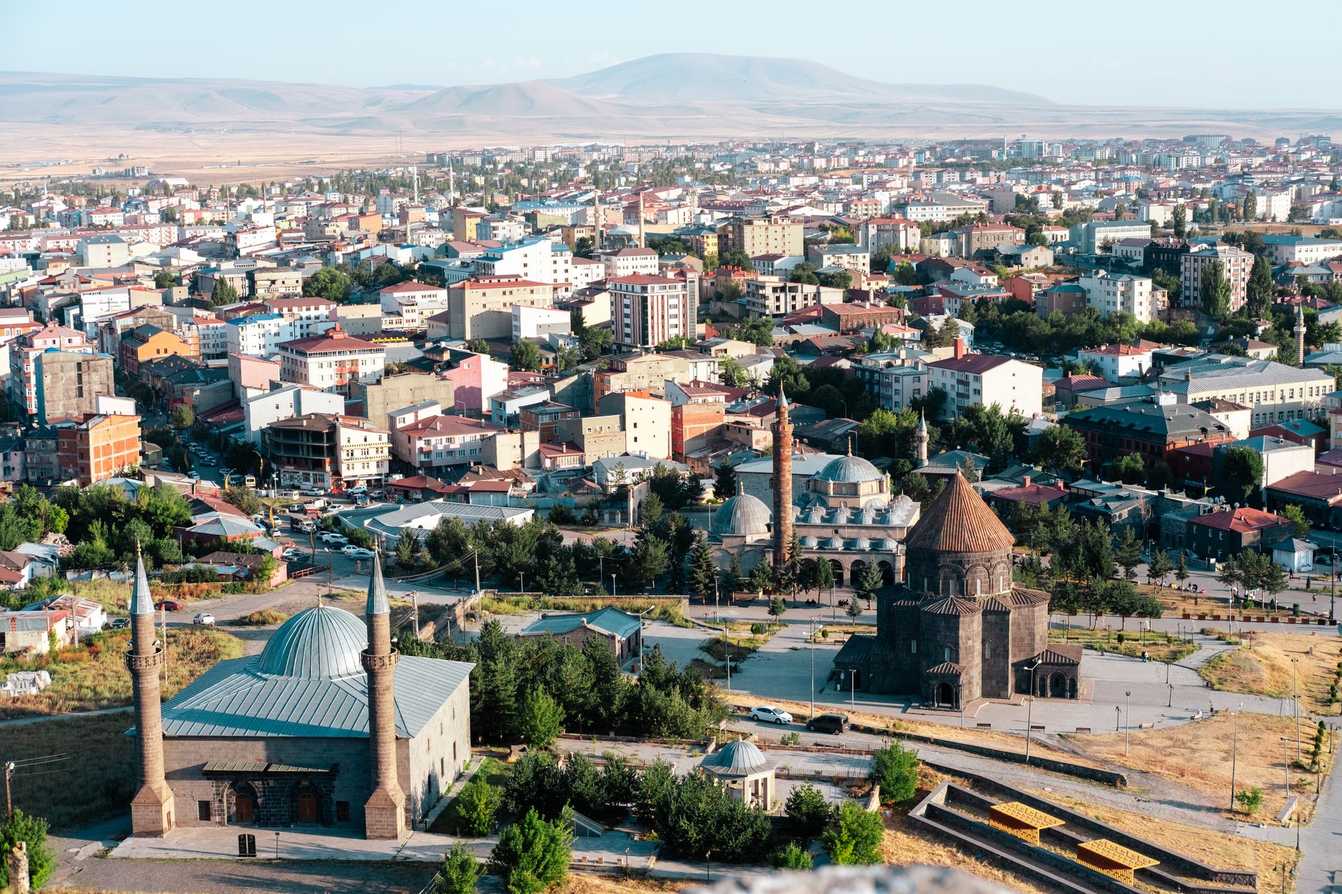Aerial view of Kars city featuring historic buildings, mosques, and mountains in the background.