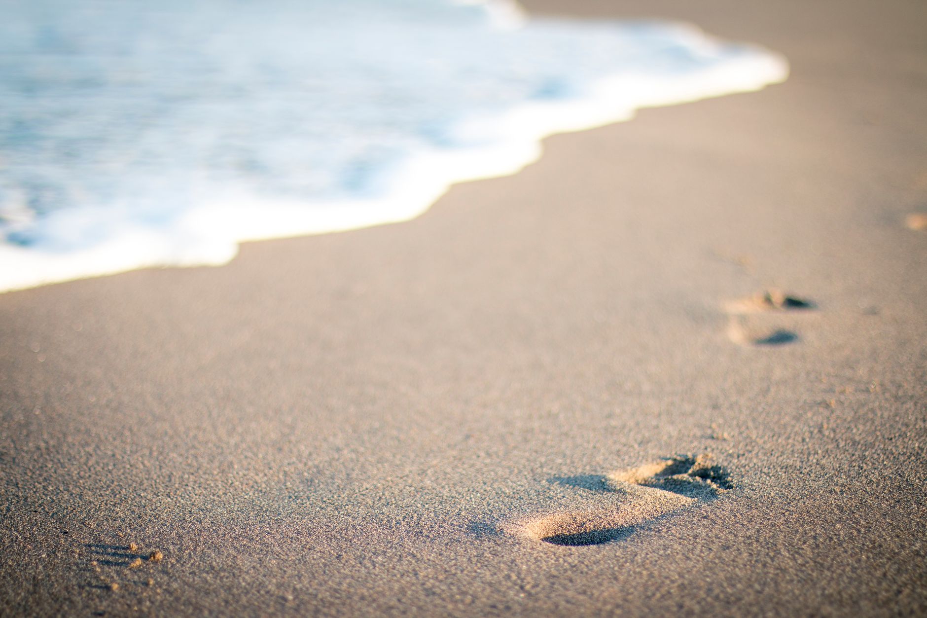 Close-up of footprints in the sand at a sunny Antalya beach with gentle waves.