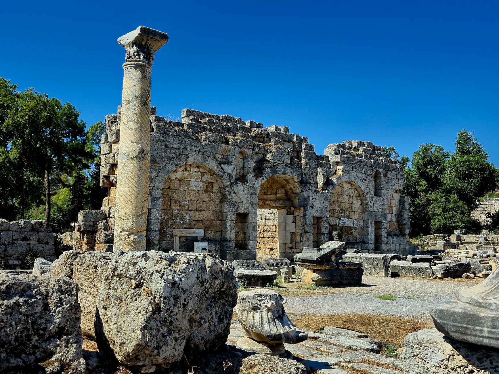 View of ancient ruins at Perge, featuring a tall column and stone structures under a clear sky.