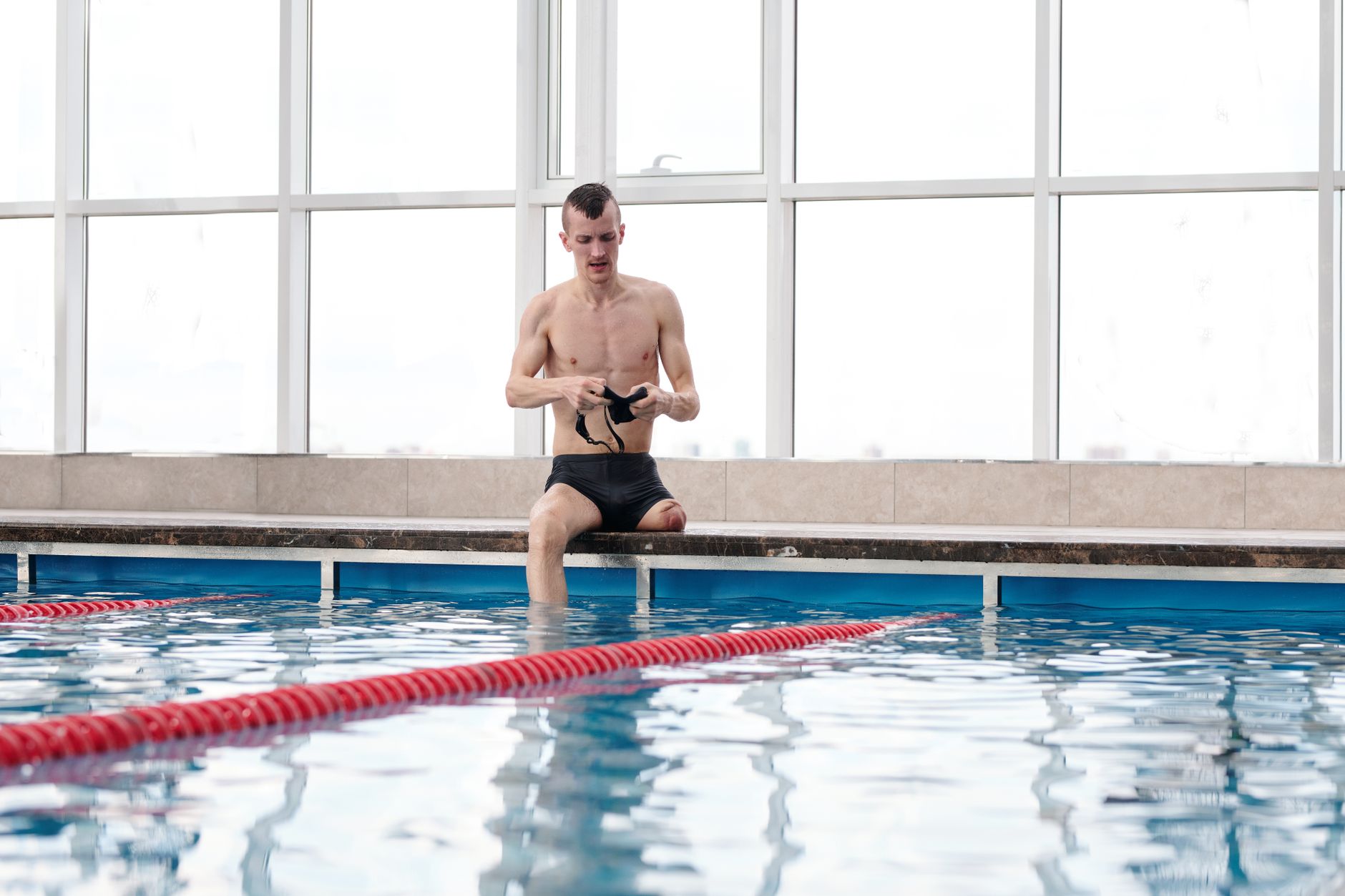 A person sits on the edge of a pool, preparing for hydrotherapy exercises in a warm indoor setting.