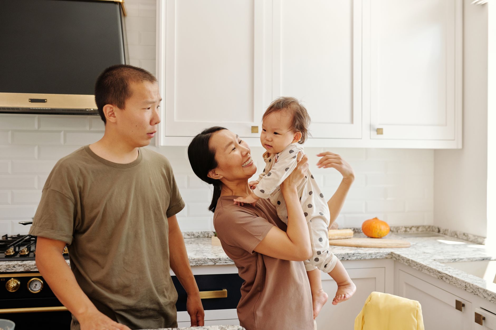 A happy couple in a modern kitchen, one holding their smiling newborn, showcasing joy after fertility treatment.