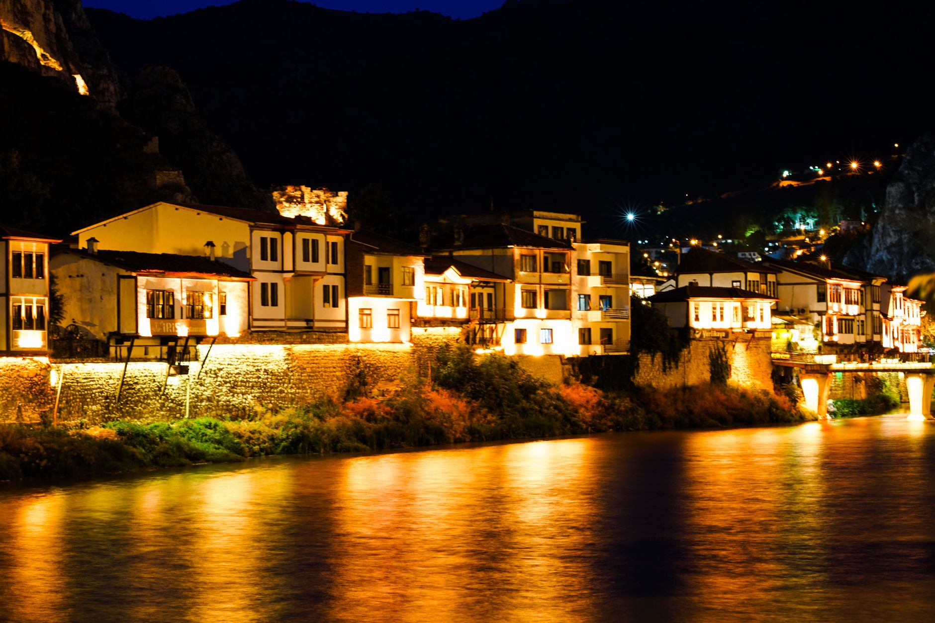 Charming illuminated houses along a river at night, reflecting warm lights.