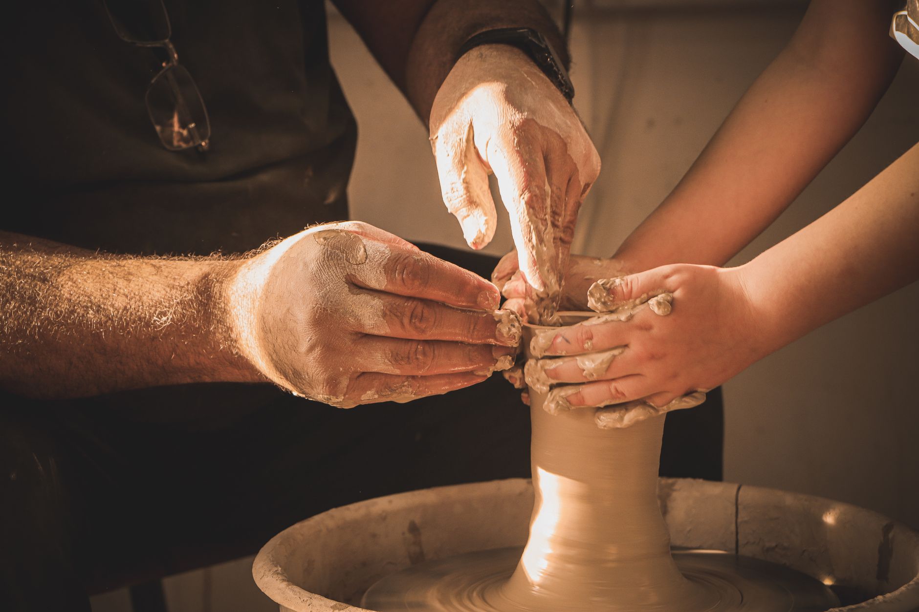 Close-up of hands covered in clay shaping a bowl on a spinning pottery wheel.
