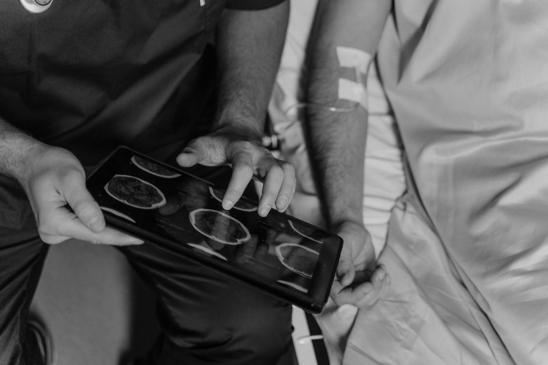 A neurosurgeon observes brain scans on a tablet while interacting with a patient.