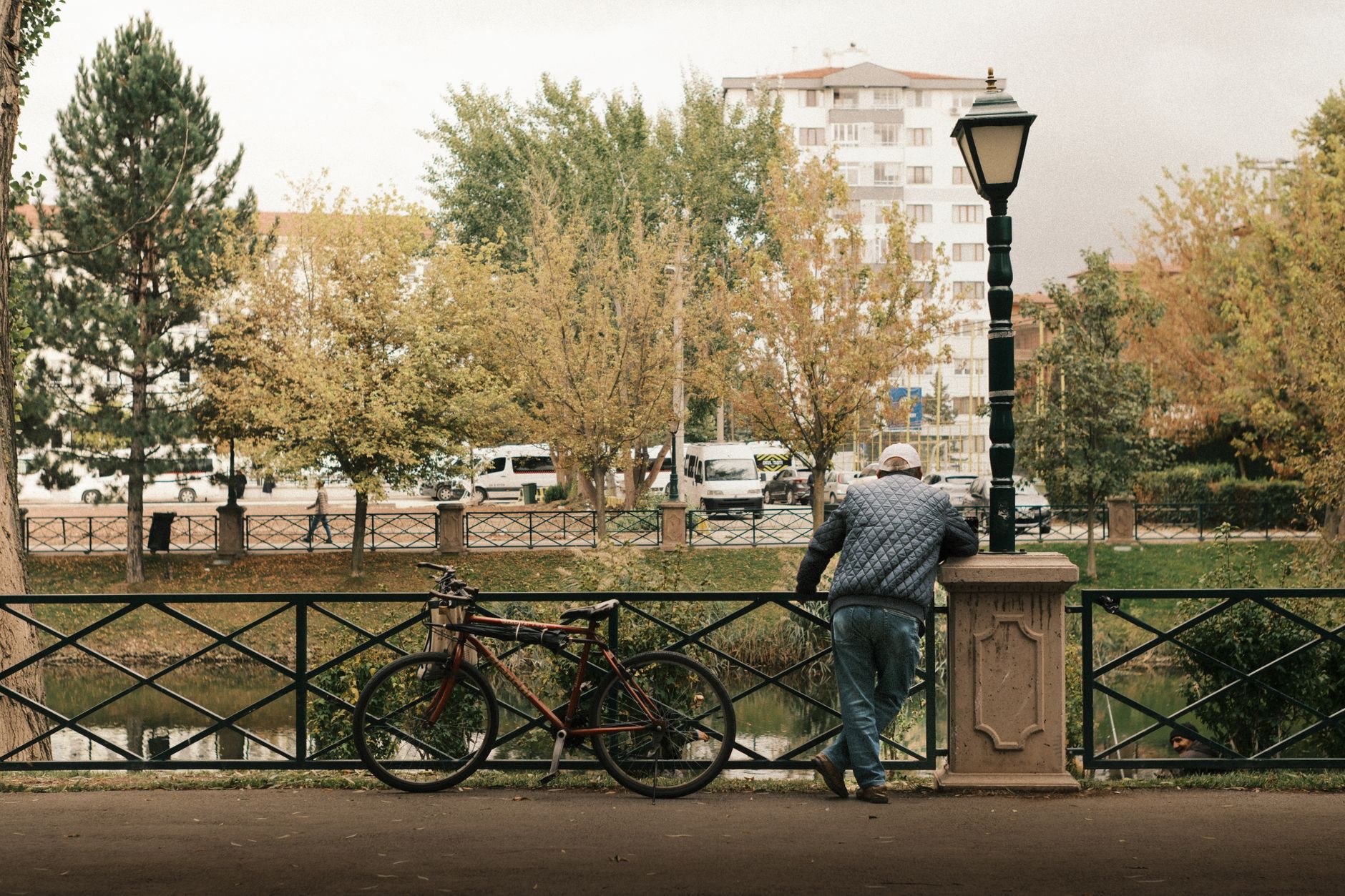 A man leans on a railing beside a bike, overlooking a serene park in Eskişehir.