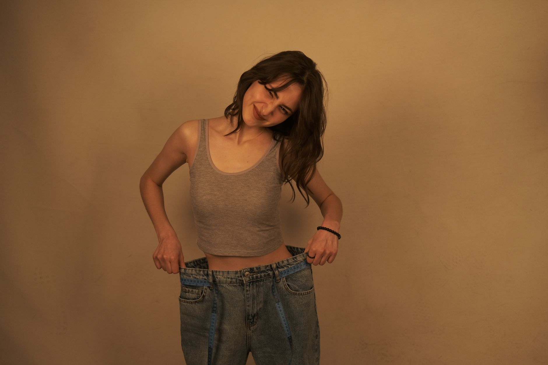 A smiling woman holds oversized jeans, showcasing her weight loss journey after bariatric surgery.