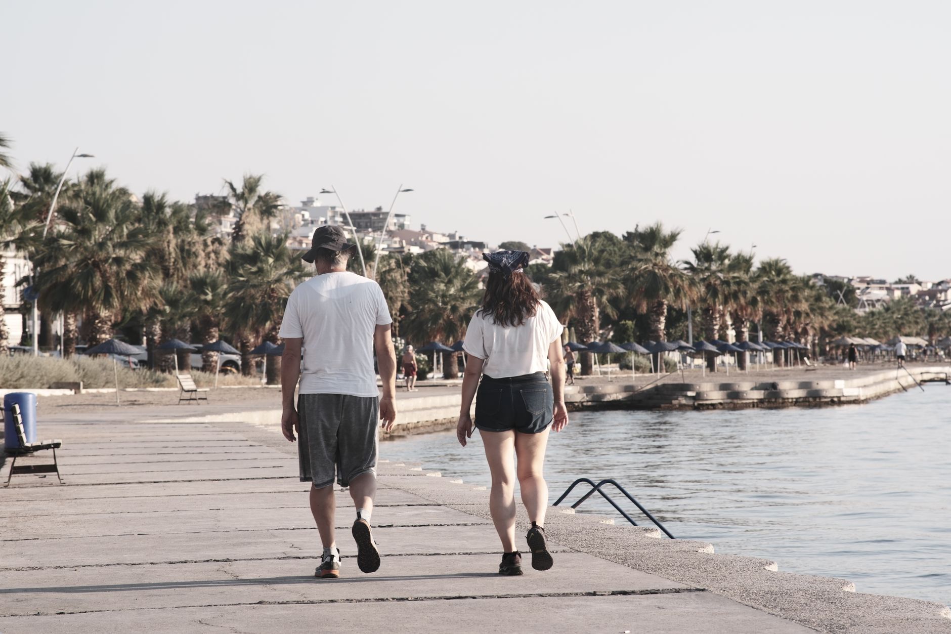 A couple walking hand in hand along Mersin's seaside promenade, surrounded by palm trees.