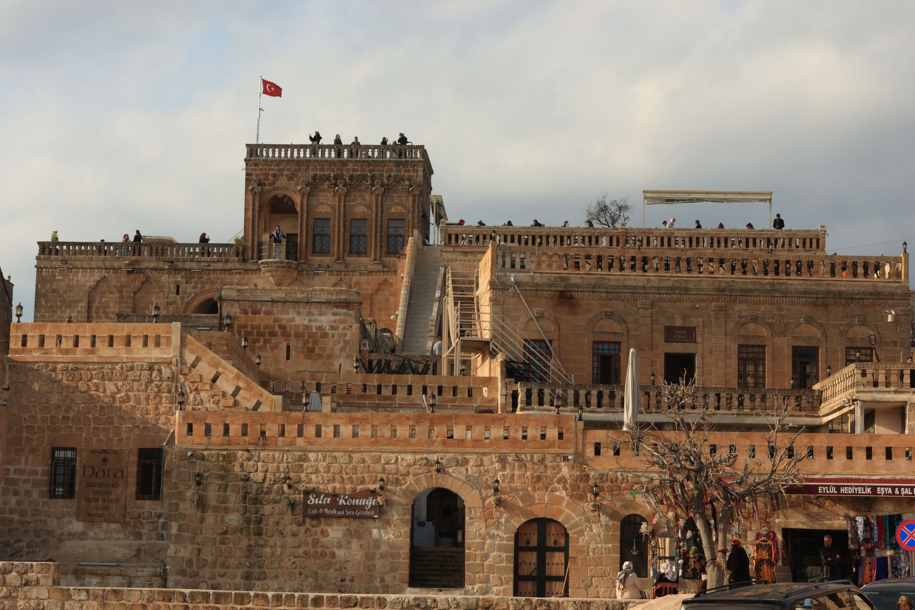 Visitors exploring Mardin's vibrant bazaar near historic limestone buildings.