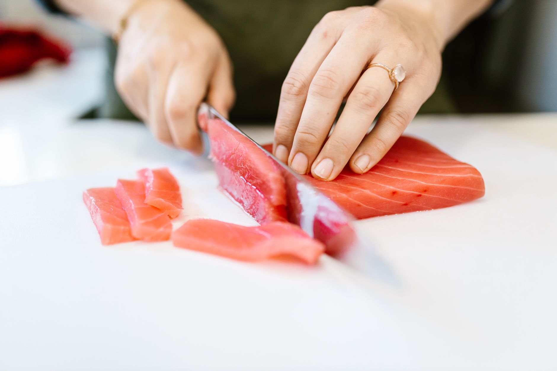 Close-up of hands slicing fresh tuna on a cutting board for meal prep.