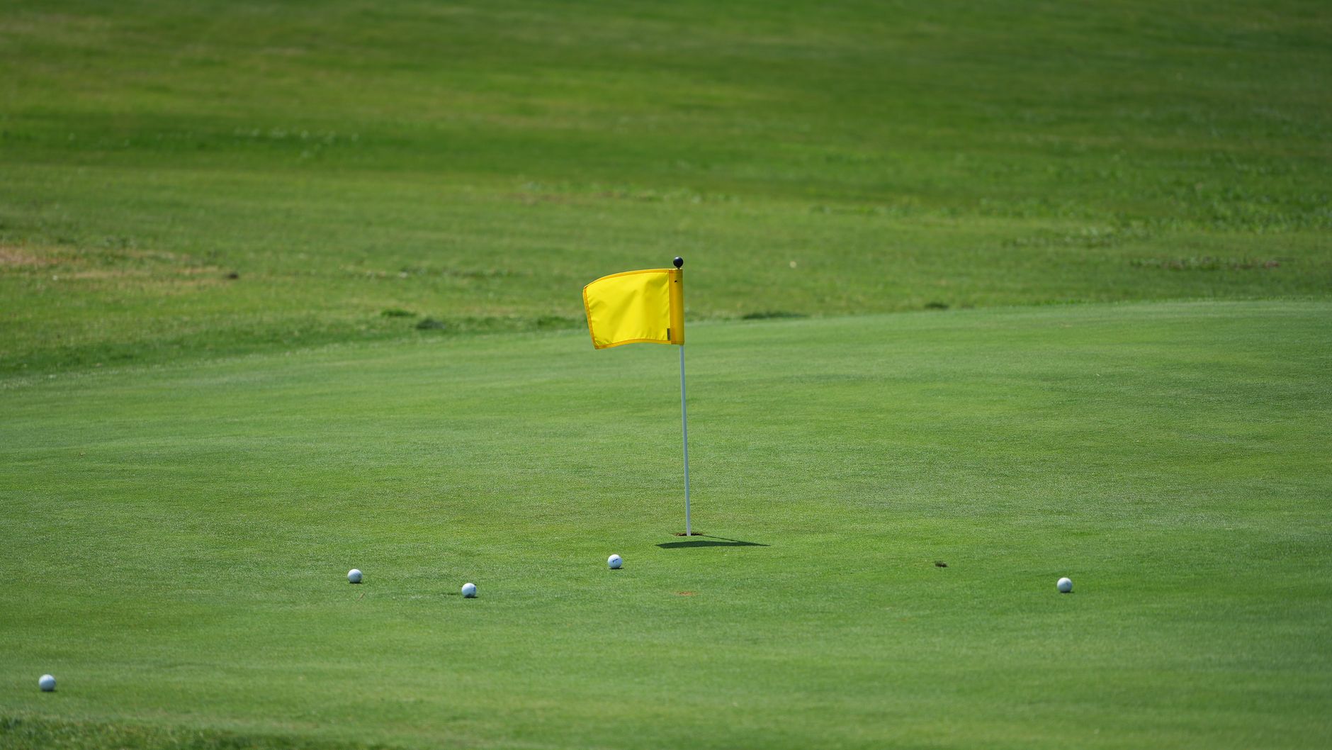 Bir golfçü bakımlı bir green üzerinde put vuruşuna hazırlanıyor; yakında sarı bir bayrak ve birkaç golf topu var.