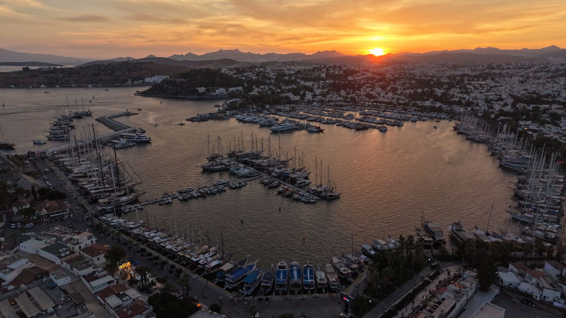 Gün batımında Bodrum Marina'nın havadan görünümü; çok sayıda yat ve sahil restoranı eşliğinde.