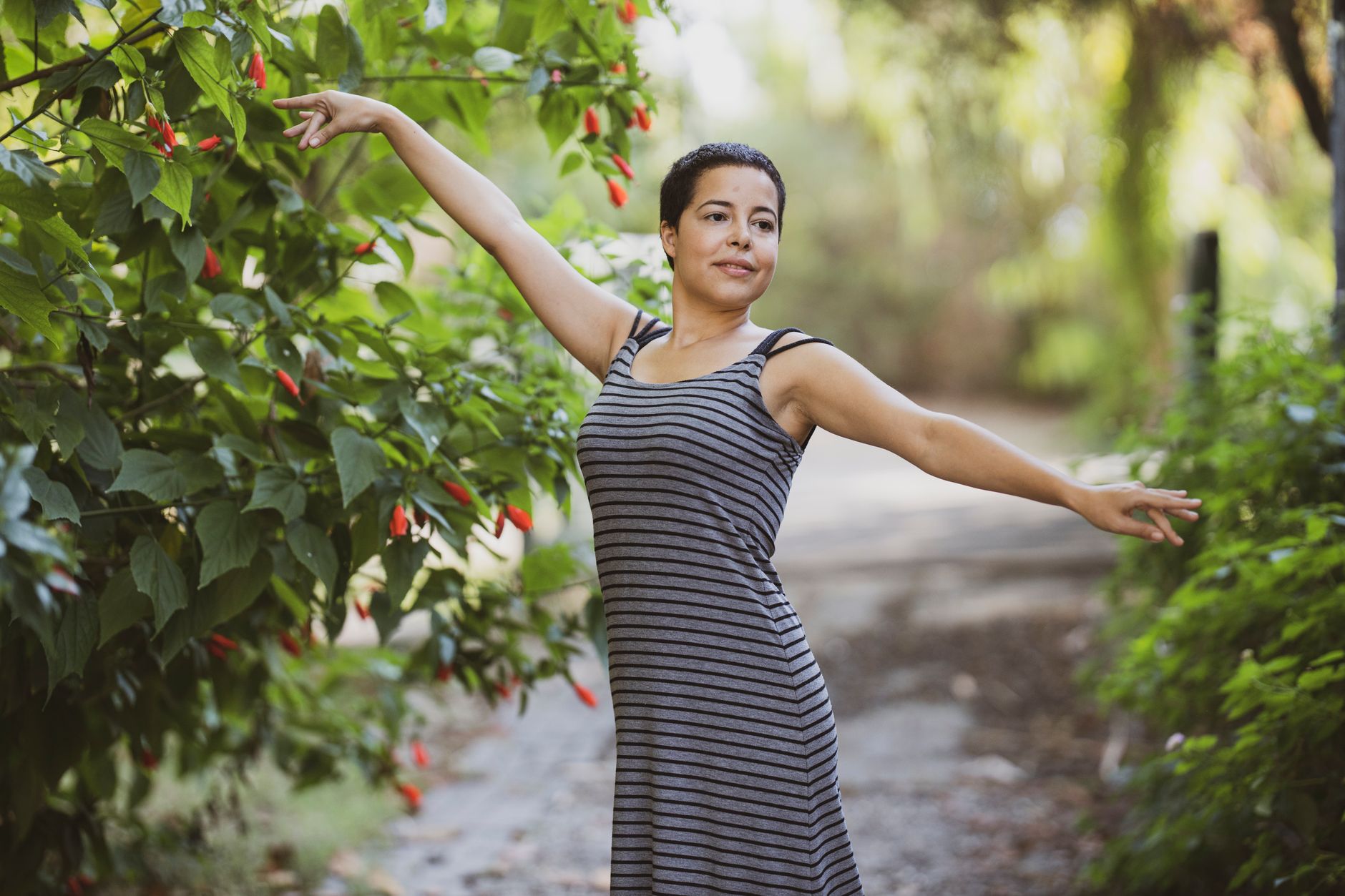 Woman in a striped dress elegantly poses outdoors among vibrant greenery.
