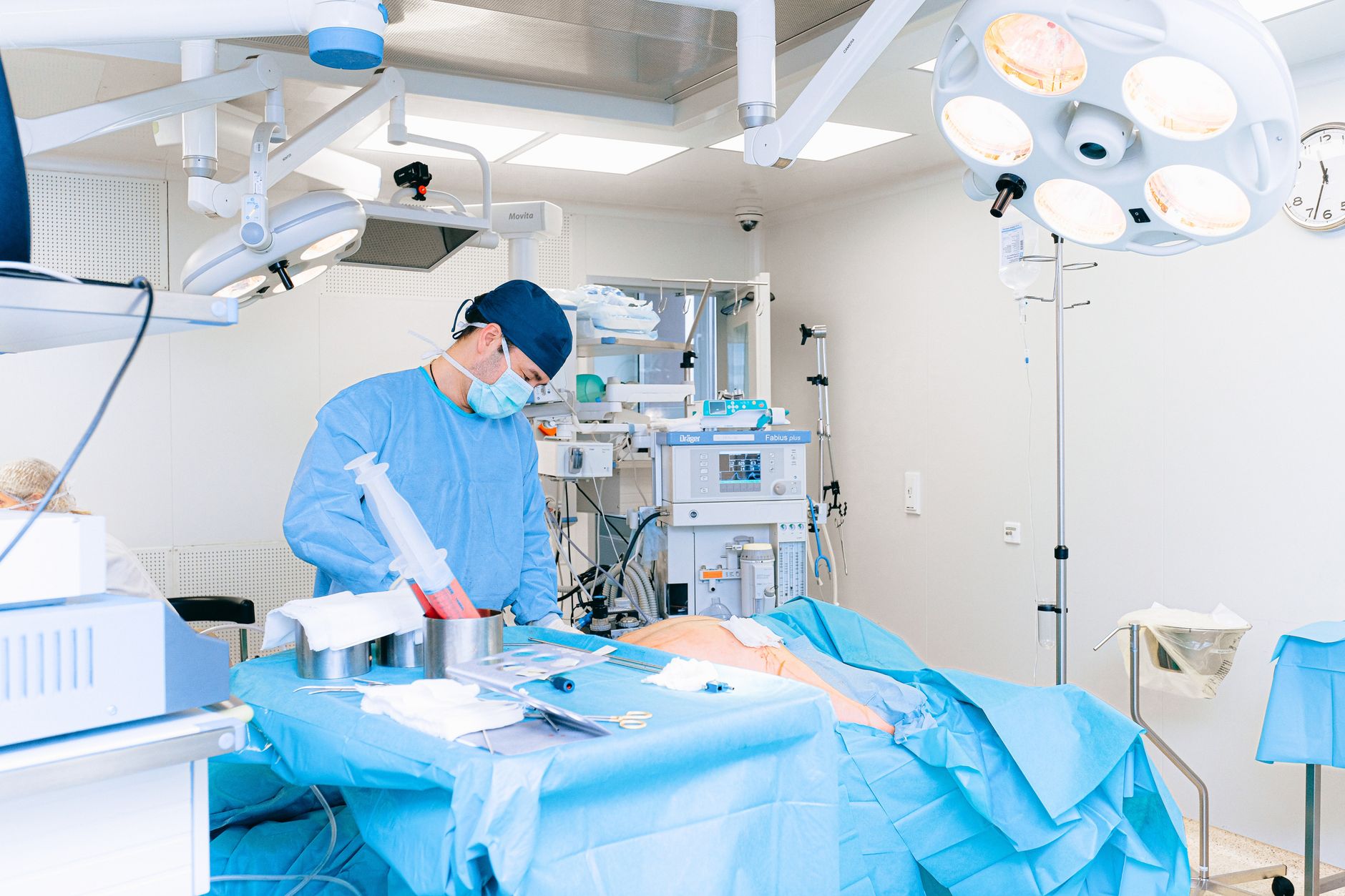 A surgeon in blue scrubs prepares for surgery in a sterile operating room.
