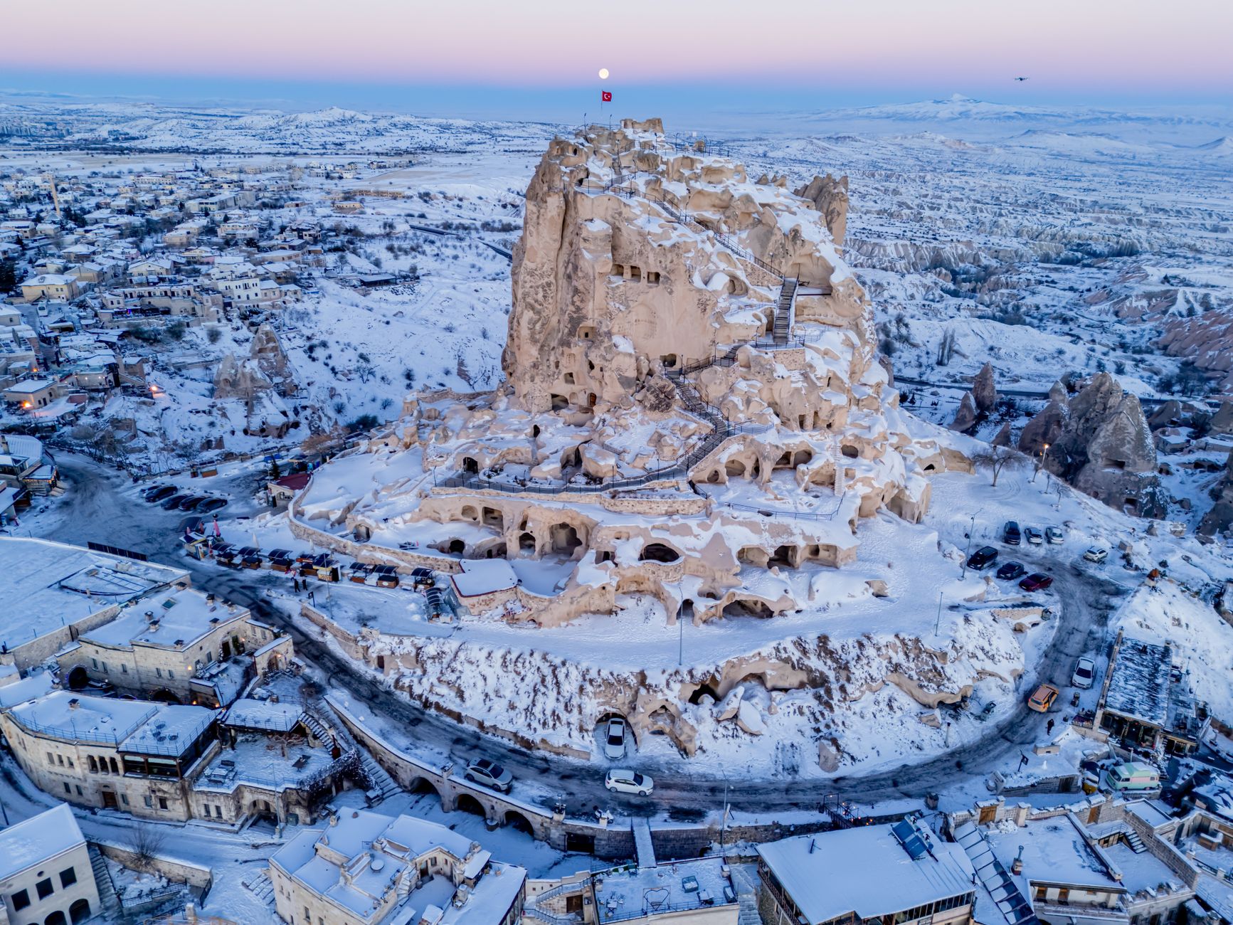被雪覆盖的乌奇希萨尔城堡鸟瞰图，展现卡帕多奇亚的洞穴酒店和独特岩层。