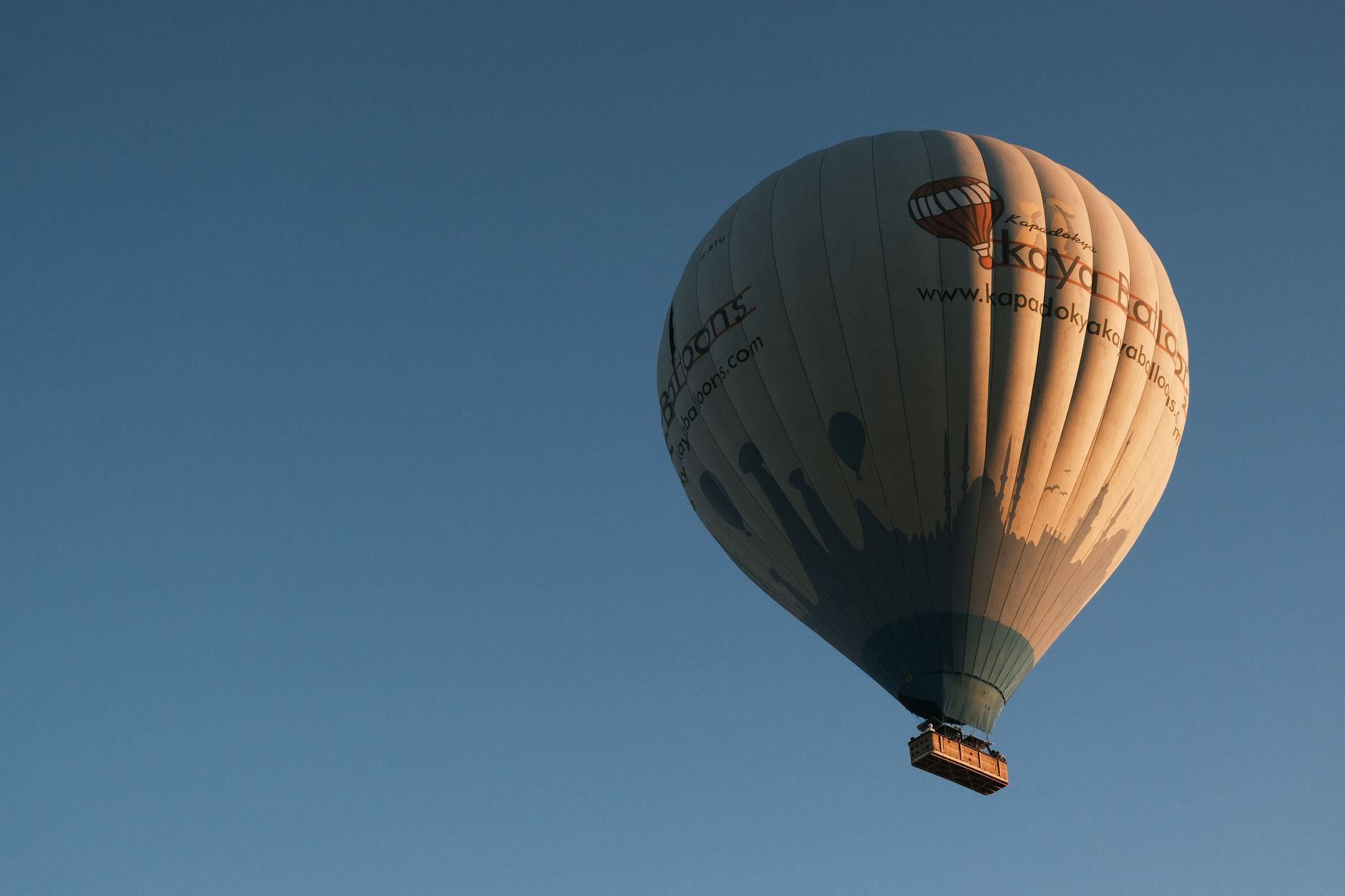 A hot air balloon floats over Cappadocia valleys at dawn, showcasing its colorful basket and burner.