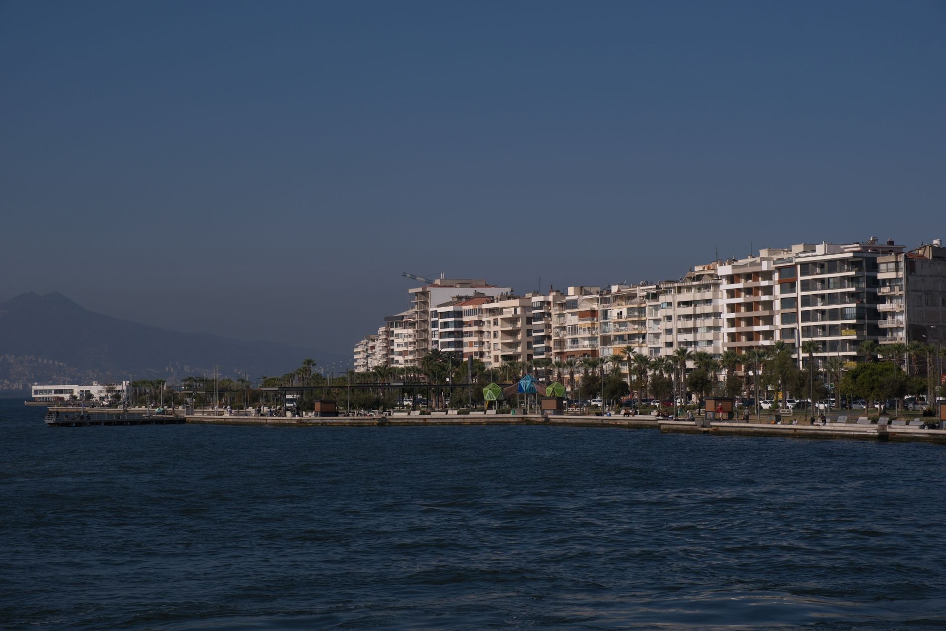 A peaceful seaside promenade in Mersin, featuring palm trees and residential buildings, perfect for walks.
