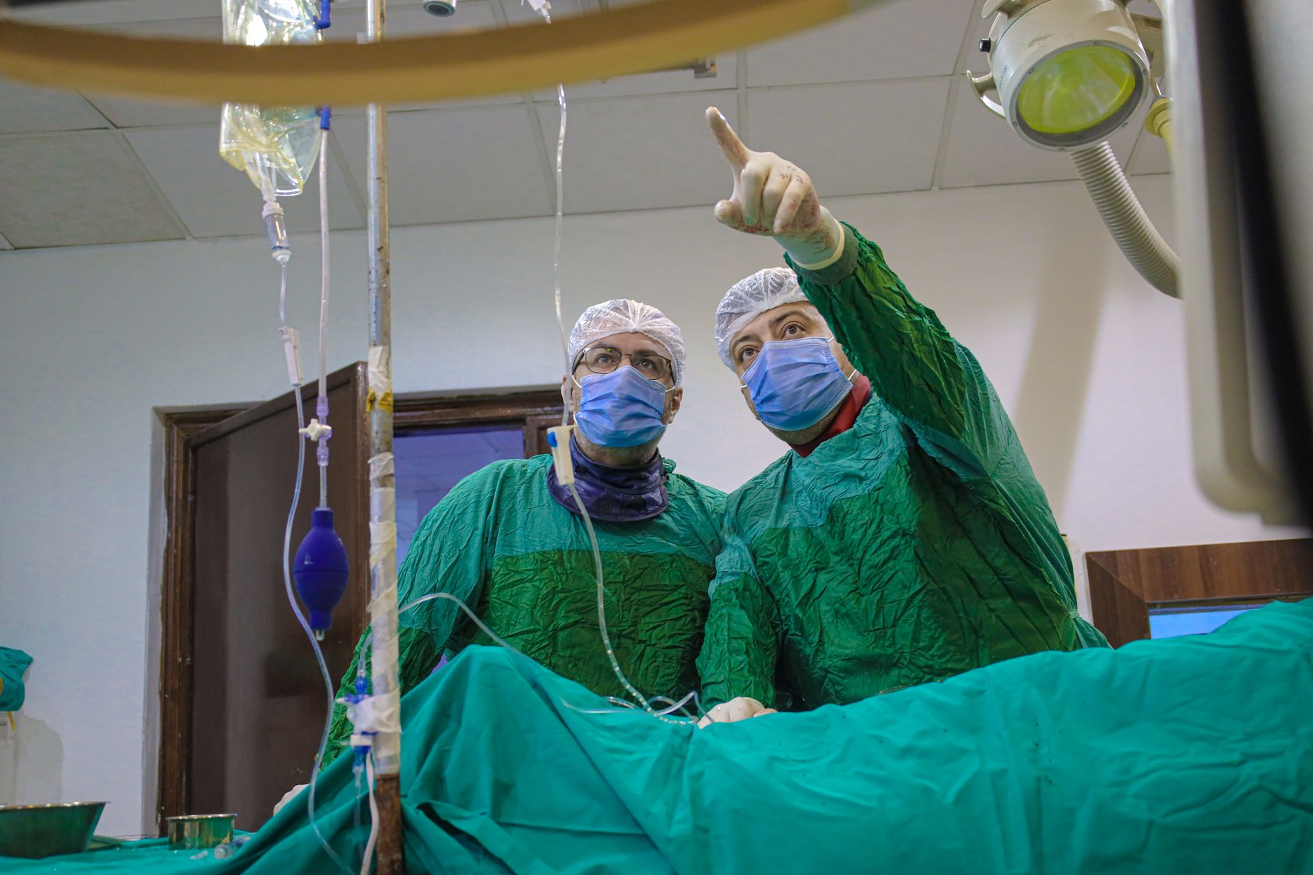 Surgeons in green scrubs and masks engaged in a cardiac procedure in a catheterisation lab, showcasing advanced technology.