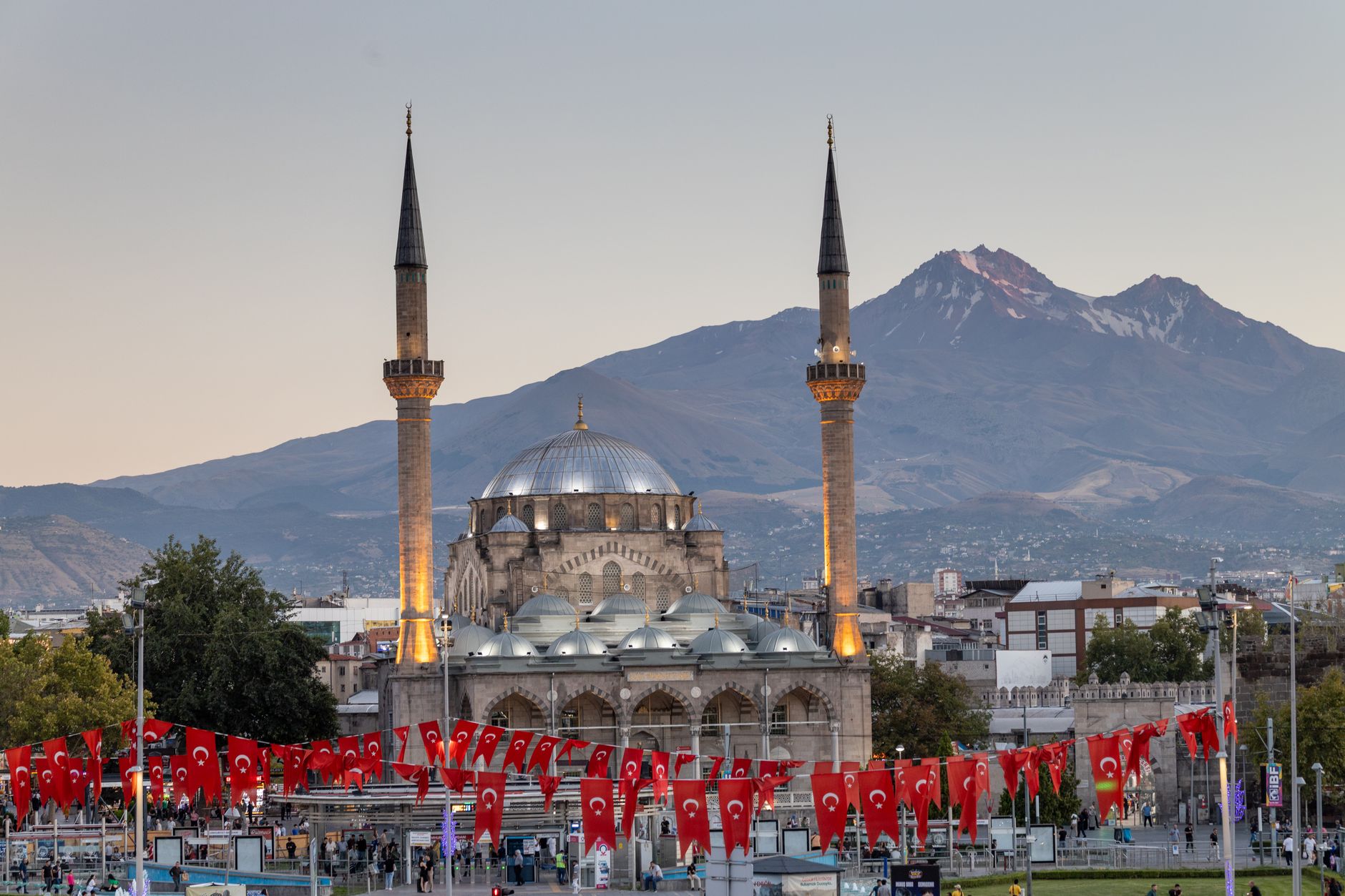 Panoramic view of Kayseri featuring a mosque and Erciyes Mountain at dusk.