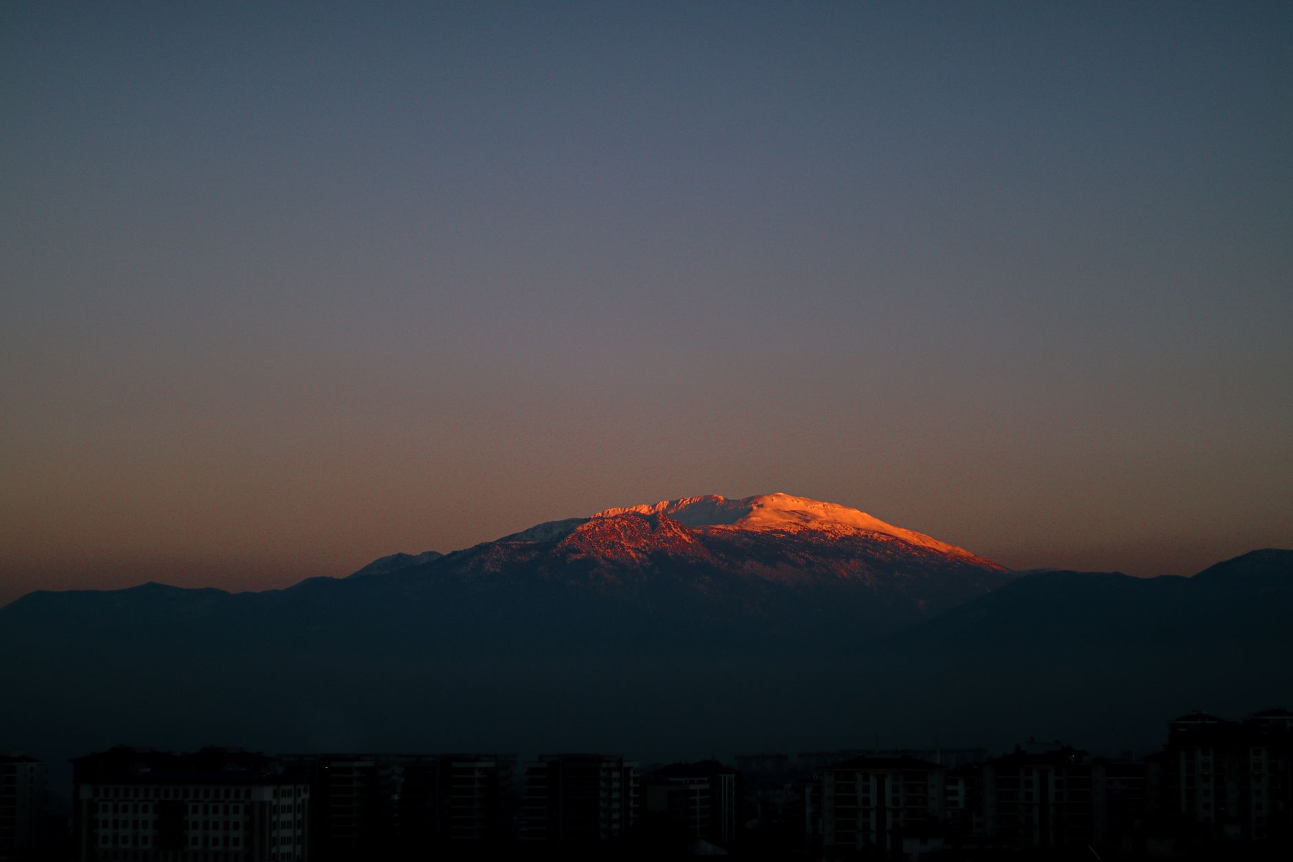 Scenic view of snow-capped mountains at sunset, overlooking Denizli's urban landscape.