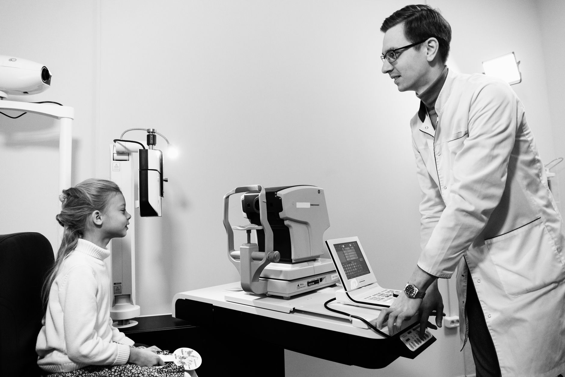 A child sits in an eye clinic, engaging with a doctor during an eye exam.