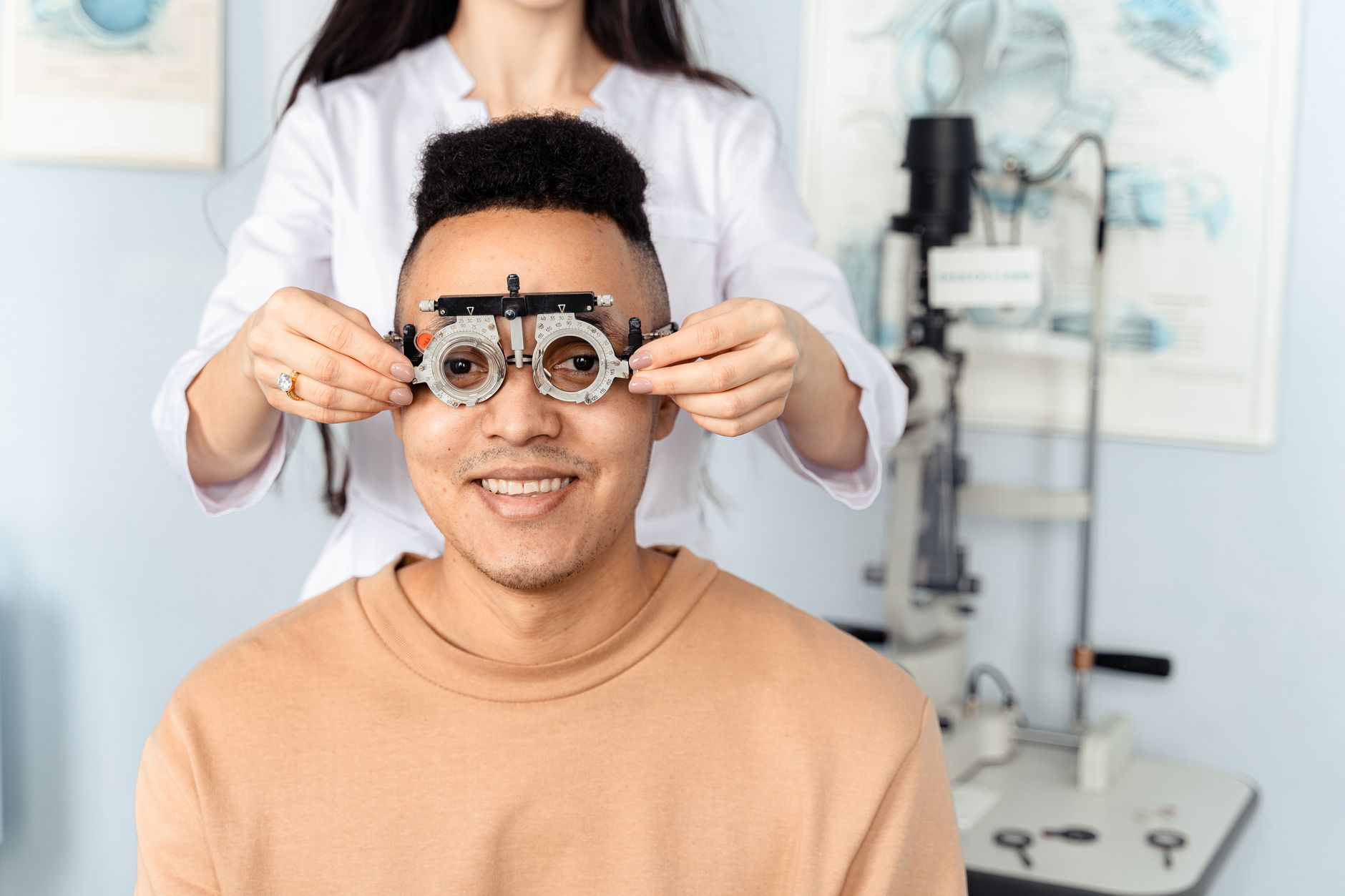 A man smiles as an optometrist adjusts a phoropter during a vision check.
