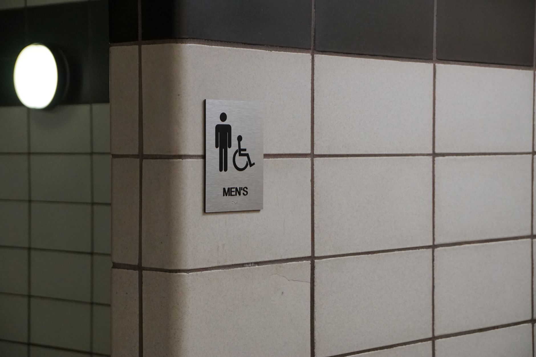 Sign for men's bathroom with wheelchair accessibility features in a hotel.
