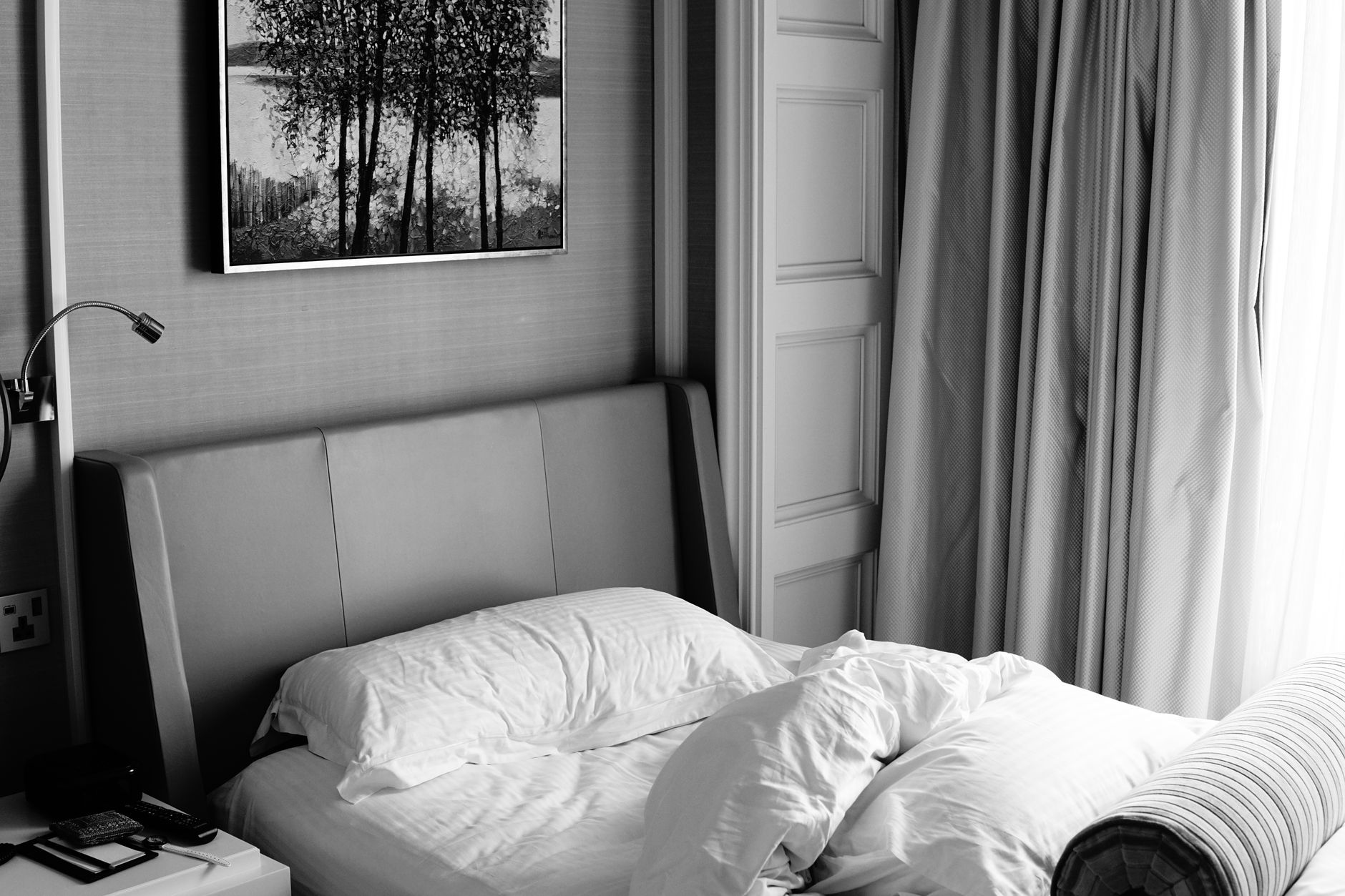 A tranquil hotel room featuring a made bed, artwork, and soft curtains.