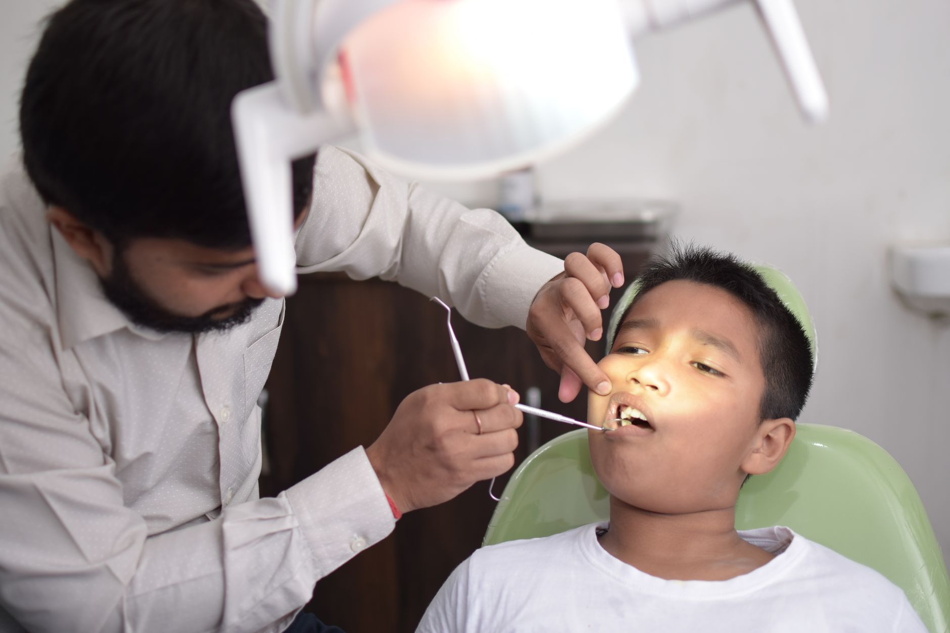 A child patient in a dental chair being examined by a dentist in a pediatric setting.