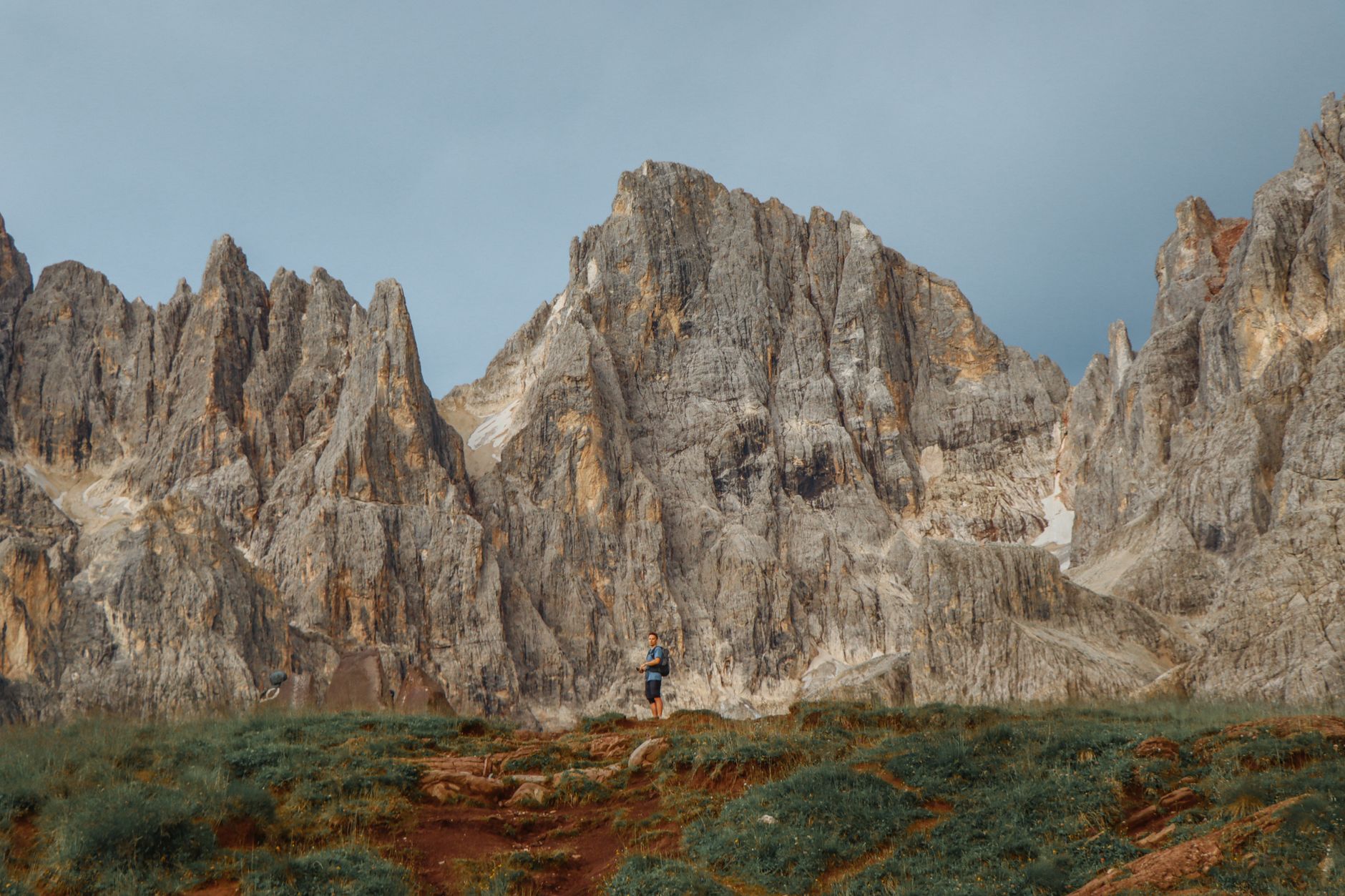 A hiker stands on a grassy trail in the Cilo-Sat Mountains, towering peaks in the background.