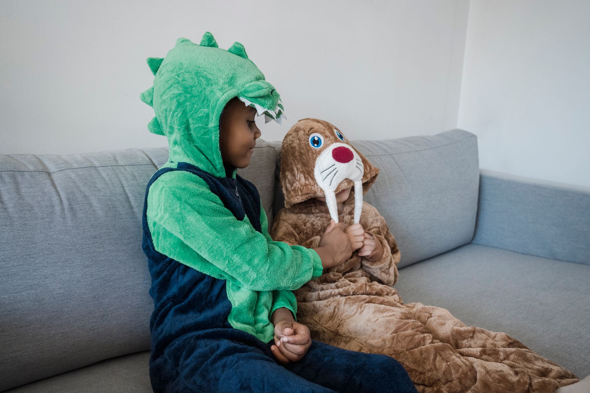 Two siblings in playful costumes relaxing on a couch in a hospital waiting area.