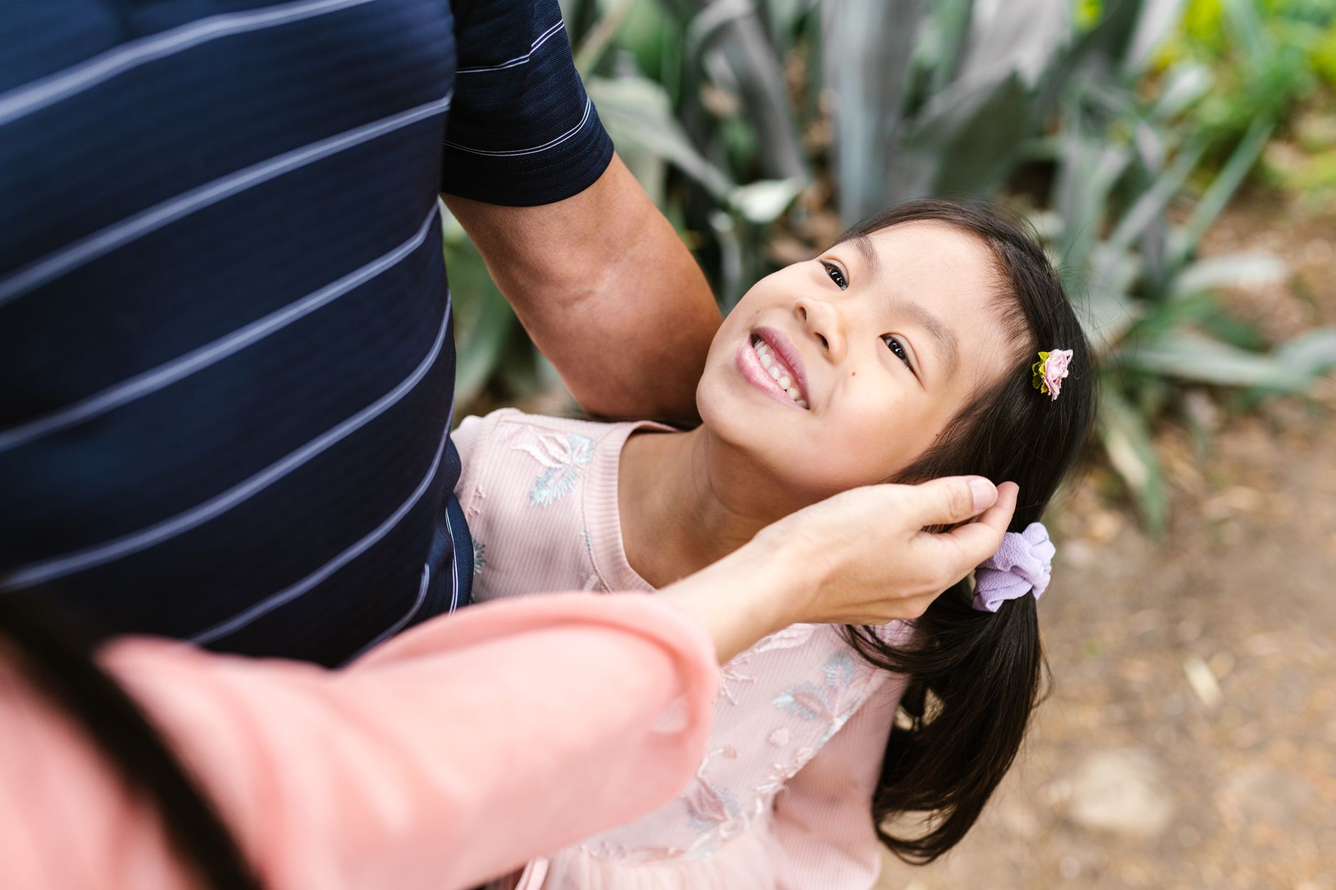 A smiling child interacts with a parent during a speech therapy session in a green outdoor setting.