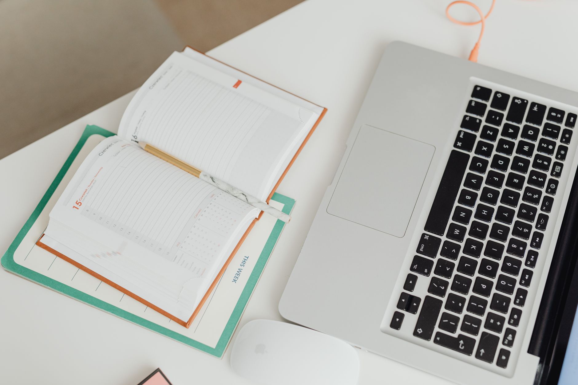 An organized desk with a planner, laptop, and mouse, ideal for scheduling and family logistics.
