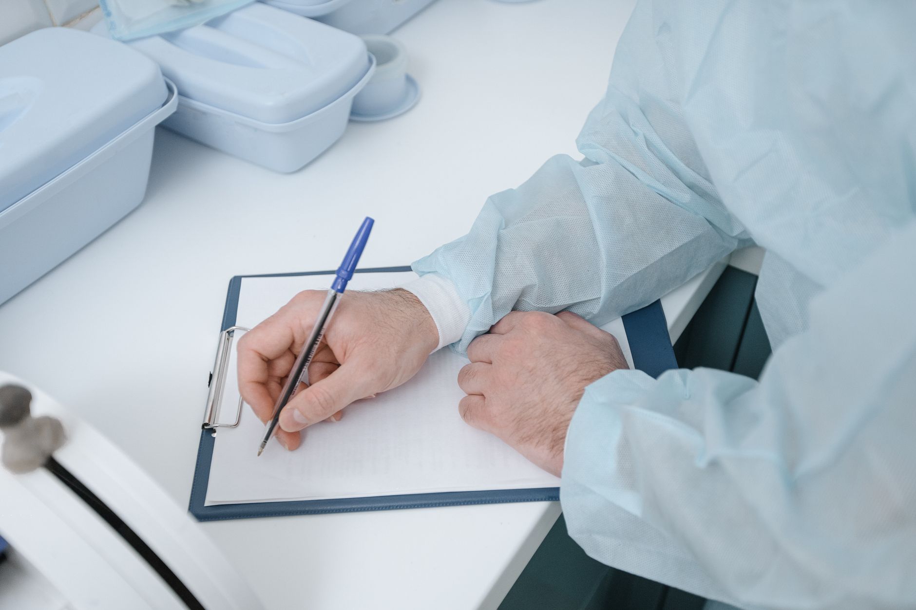 Hands in medical attire writing on a clipboard at a clinic.
