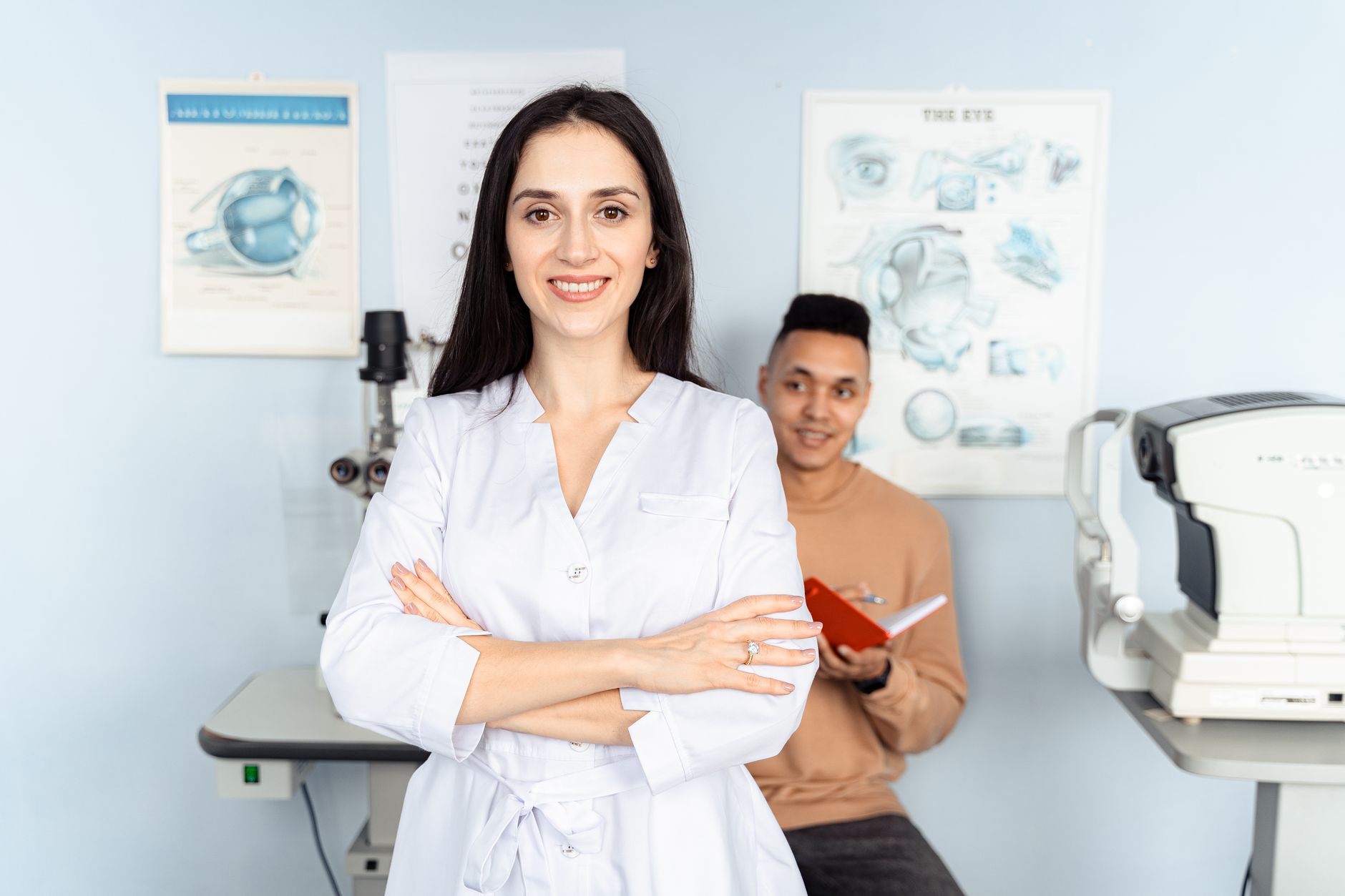 A female optometrist stands confidently with arms crossed, while a male patient reviews notes in a modern clinic.