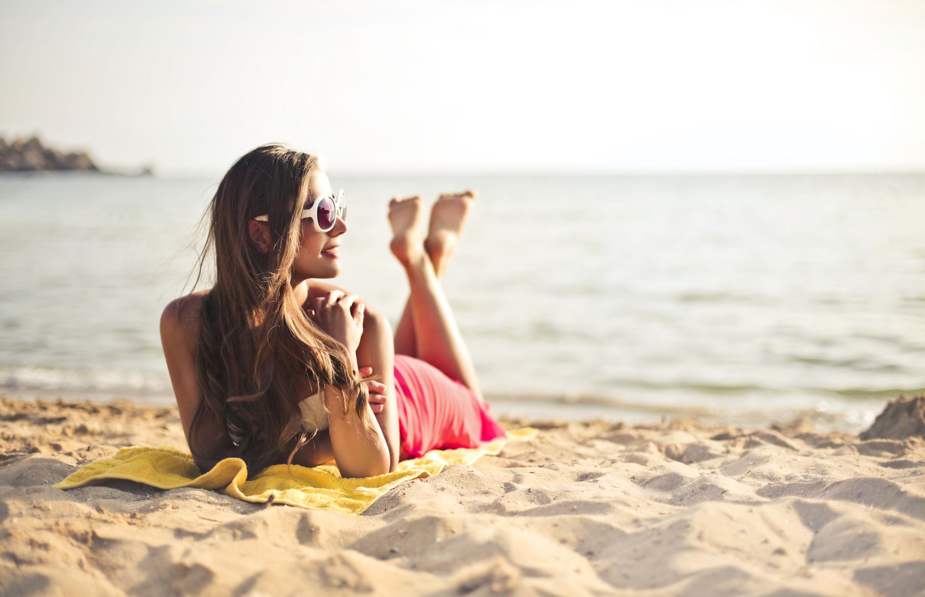 A woman in sunglasses lounges on a yellow towel at Mersin beach, enjoying the peaceful seaside view.