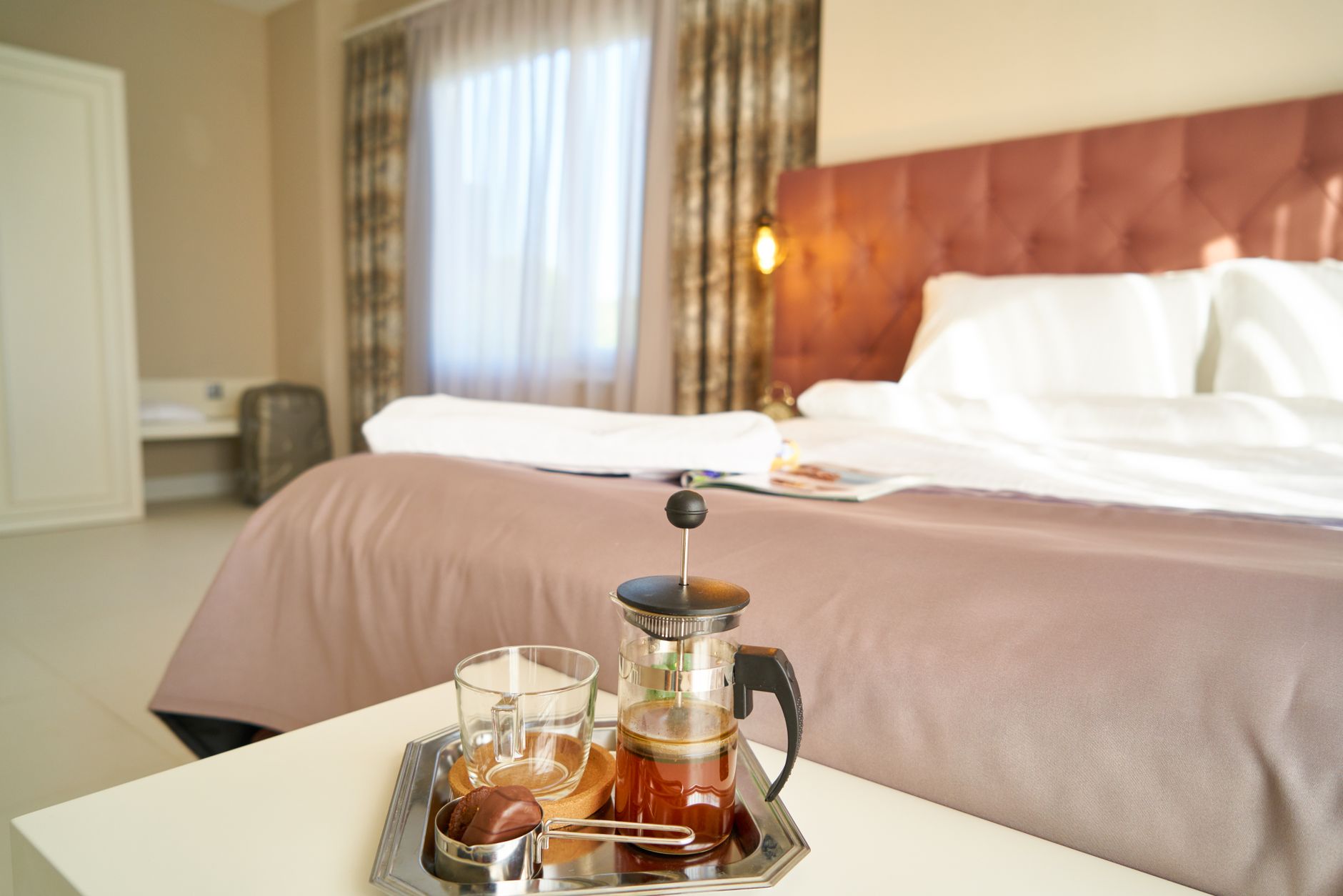 A cozy hotel room with a bed, tea service, and natural light, ideal for relaxation.