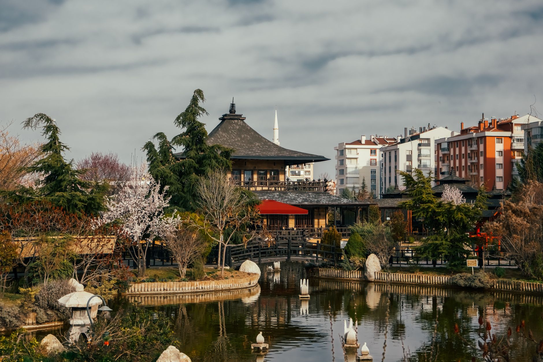 A peaceful garden in Konya featuring a traditional building, greenery, and a pond.