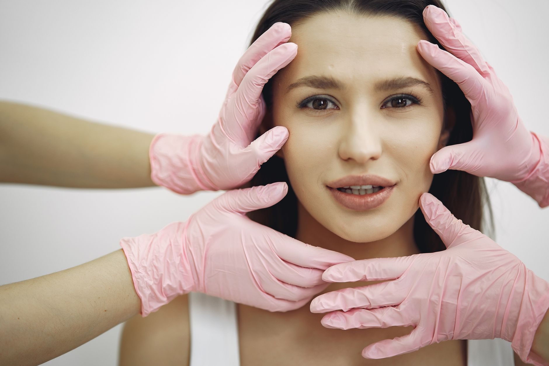 A woman receiving facial rejuvenation treatment with hands in pink gloves.