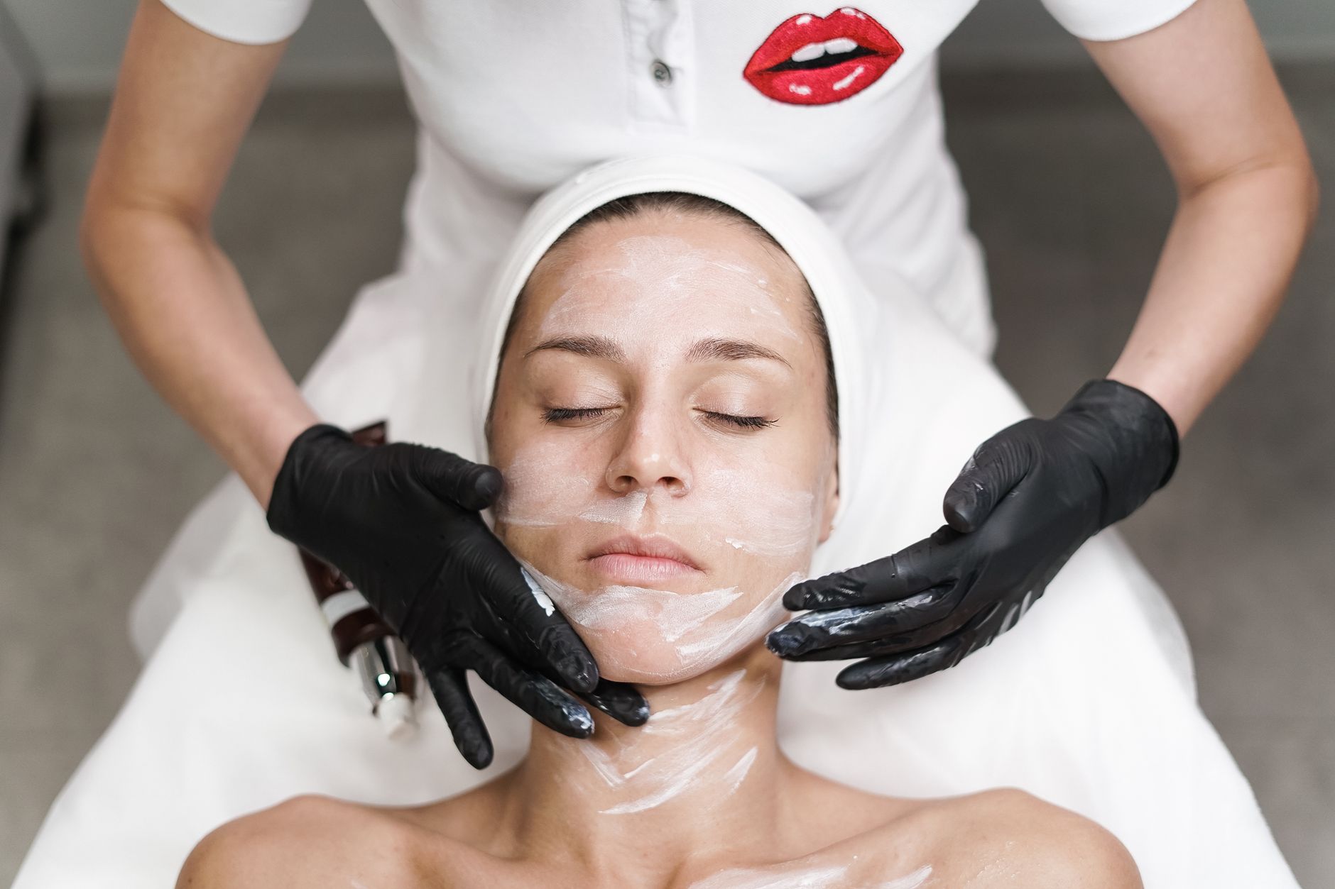 A practitioner applies a cream during a HIFU facial treatment on a woman's face.