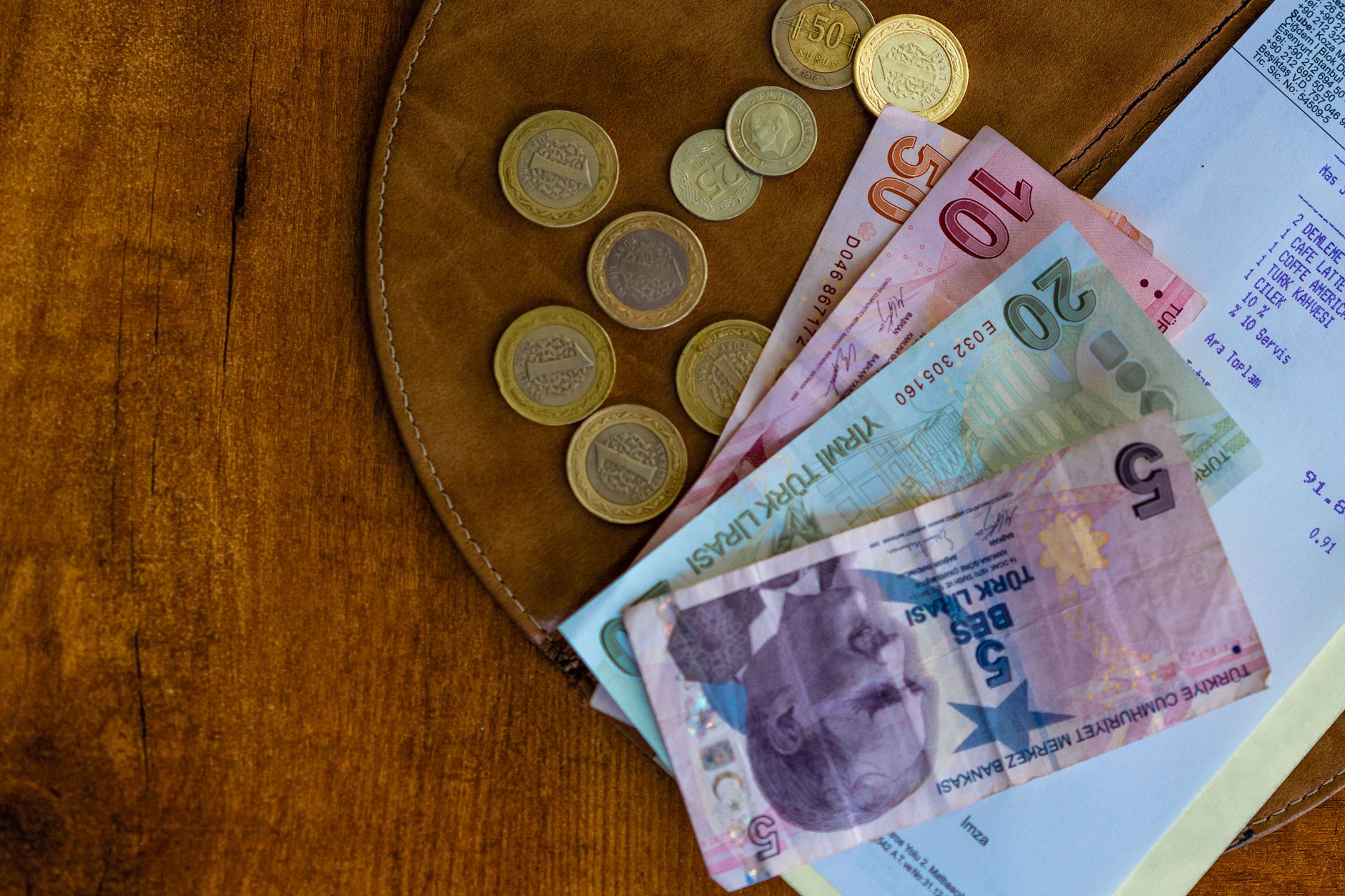 A collection of Turkish lira banknotes and coins arranged on a wooden surface.
