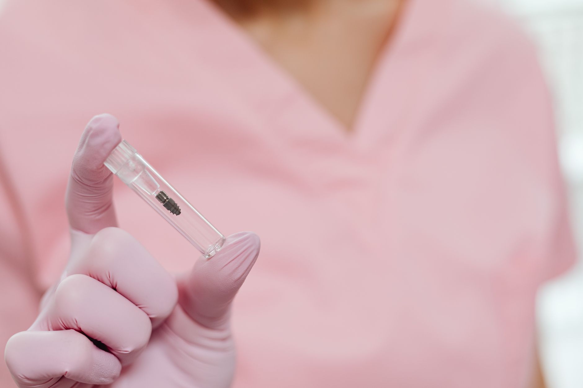 Close-up showing a dental implant in a vial held by a gloved hand.
