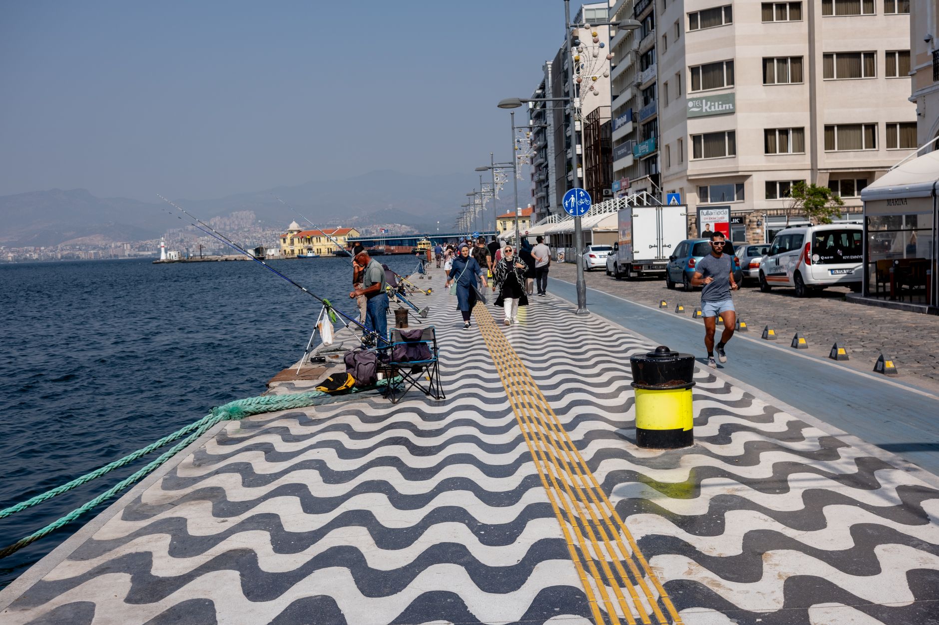 People walking and fishing along the scenic Izmir waterfront, showcasing lively promenade activities.