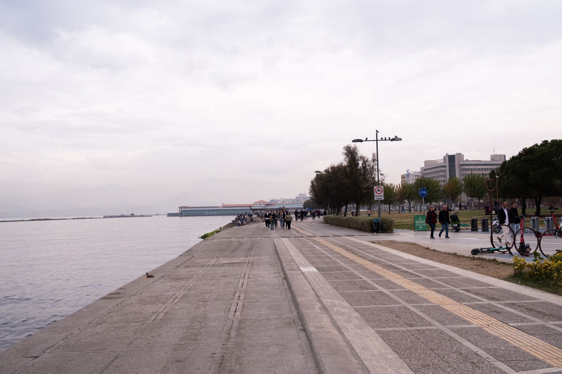 People walking and enjoying the view along Izmir's seaside promenade, with a tranquil coastal atmosphere.