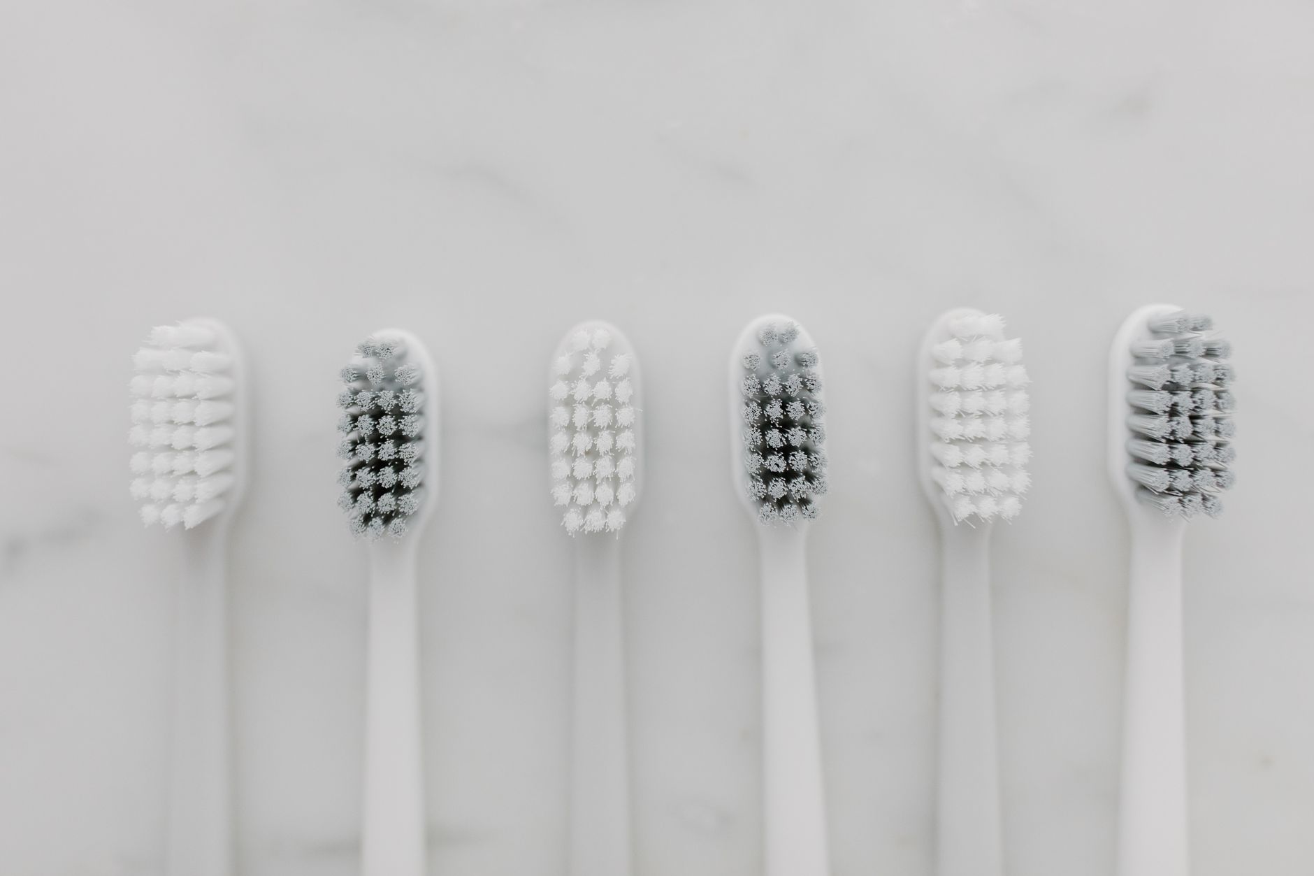 A row of six toothbrushes in varying colors on a light surface, illustrating dental care after a veneer makeover.